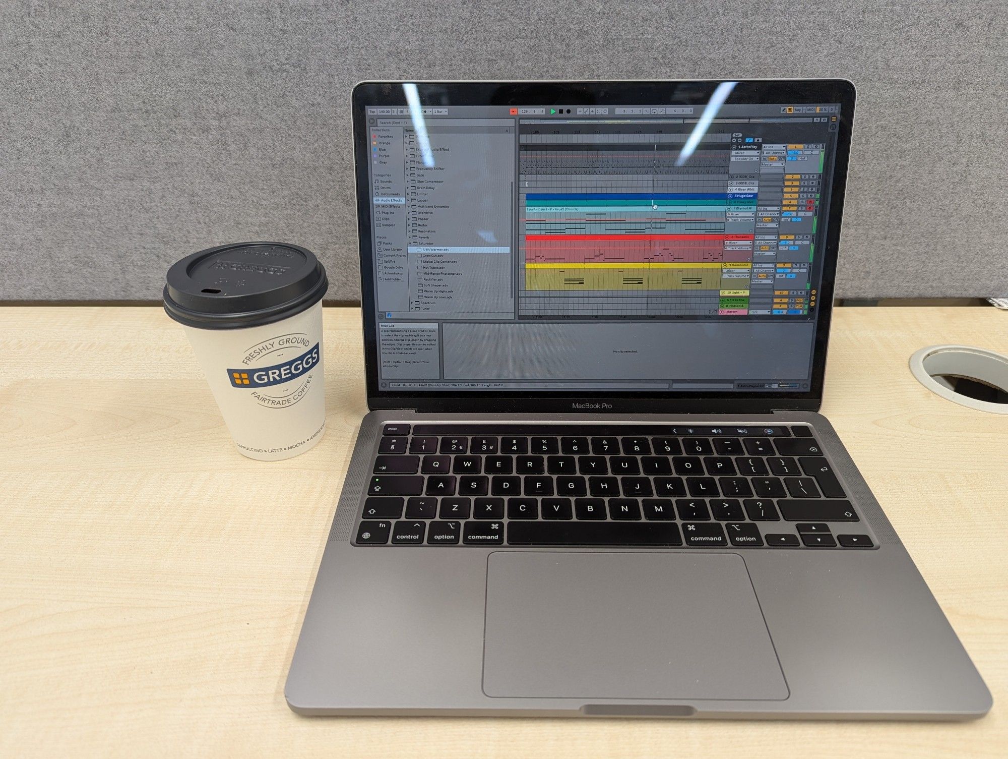 Laptop with ableton open, and a Greggs cappuccino, on a desk in a library