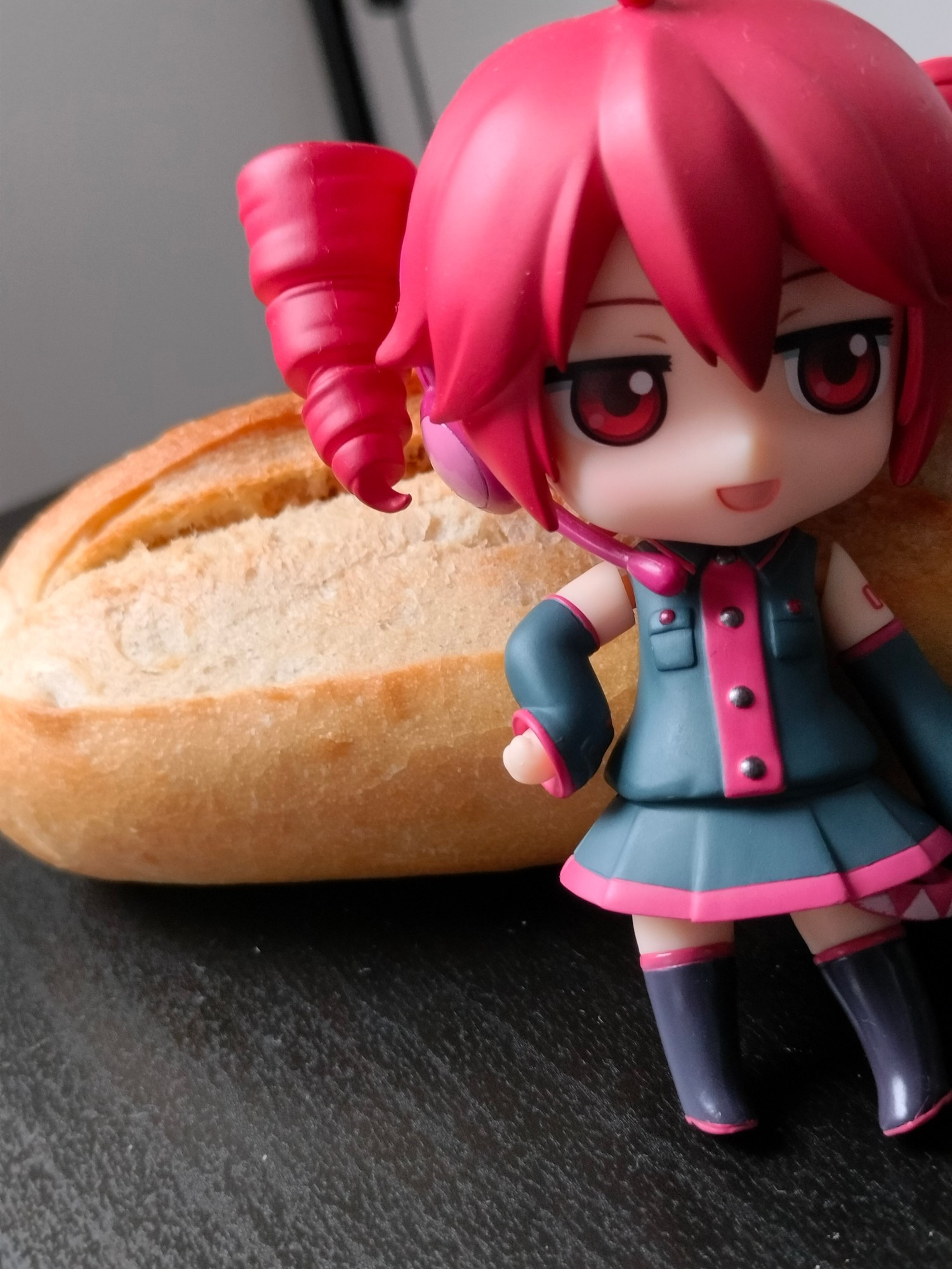 A picture of a Kasane Teto nendoroid with a baguette behind her