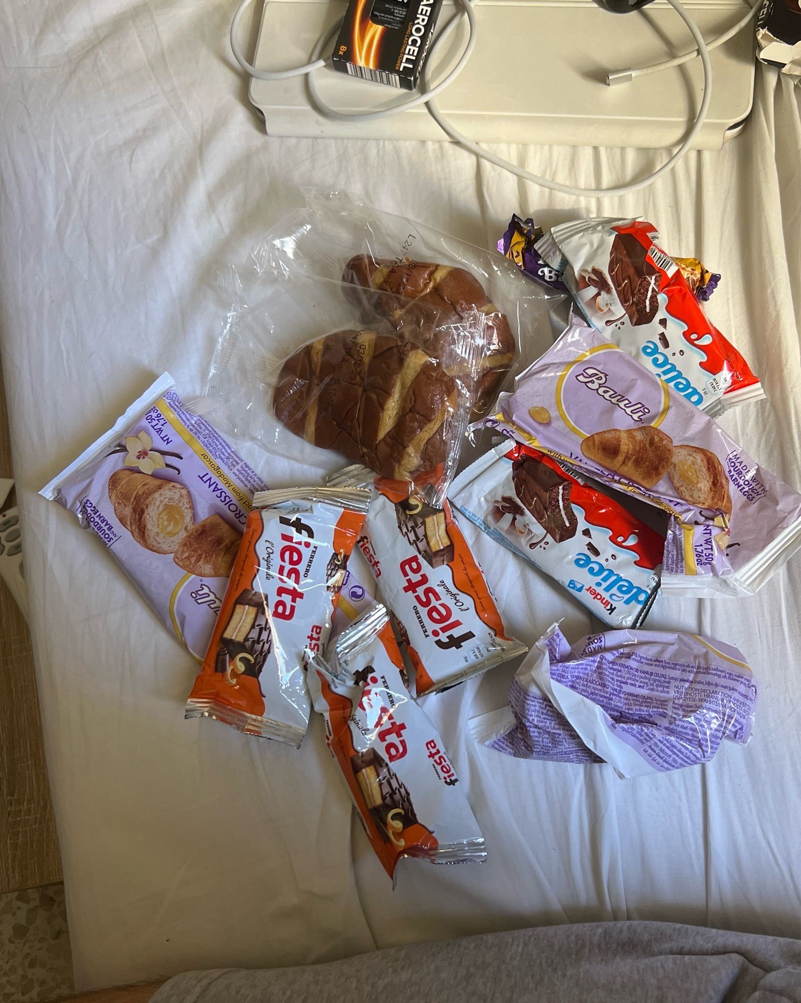 A collection of various uneaten croissants and chocolate snacks dumped on a bed