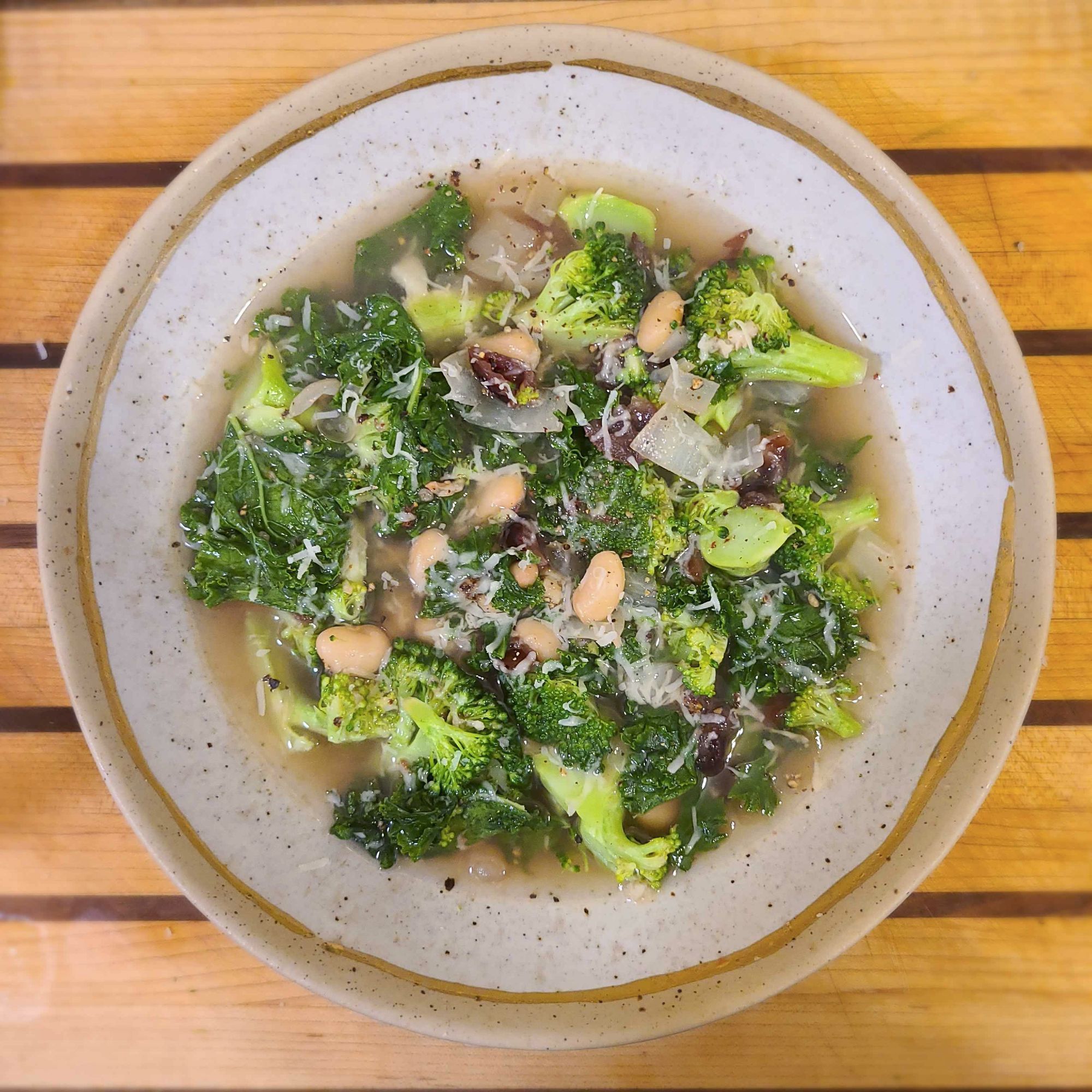 a bowl of broccoli, kale, and white bean soup with cranberries and parmesan