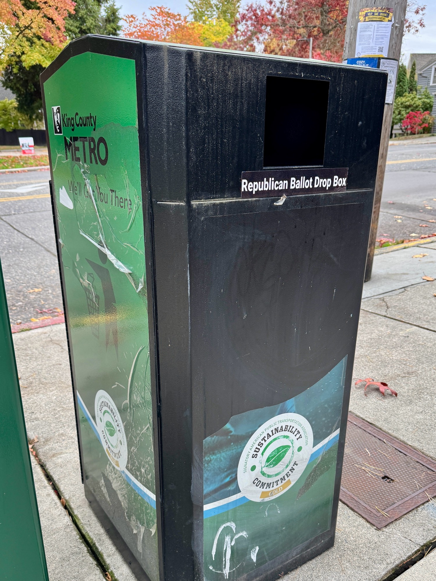 A trash bin receptacle at a bus stop with a sticker below the garbage entry hole that reads: Republican ballot dropbox