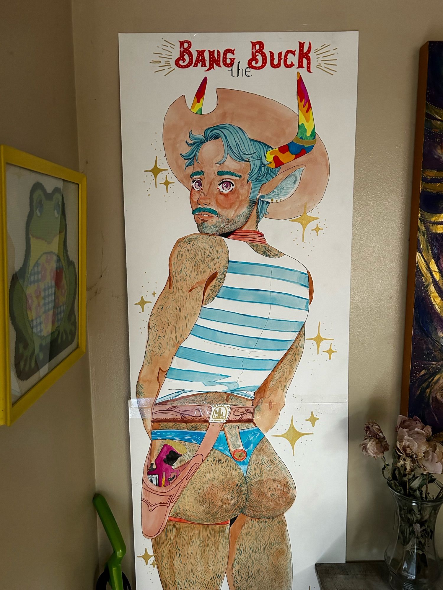 A large traditional pinup of a cowboy. He has blue hair and rainbow horns sticking out from under a large cowboy hat. His back faces the camera and he looks over his shoulder with a demure, shojo anime  look. Carnival font reads, “Bang the Buck” alluding to the cowboys exposed posterior.