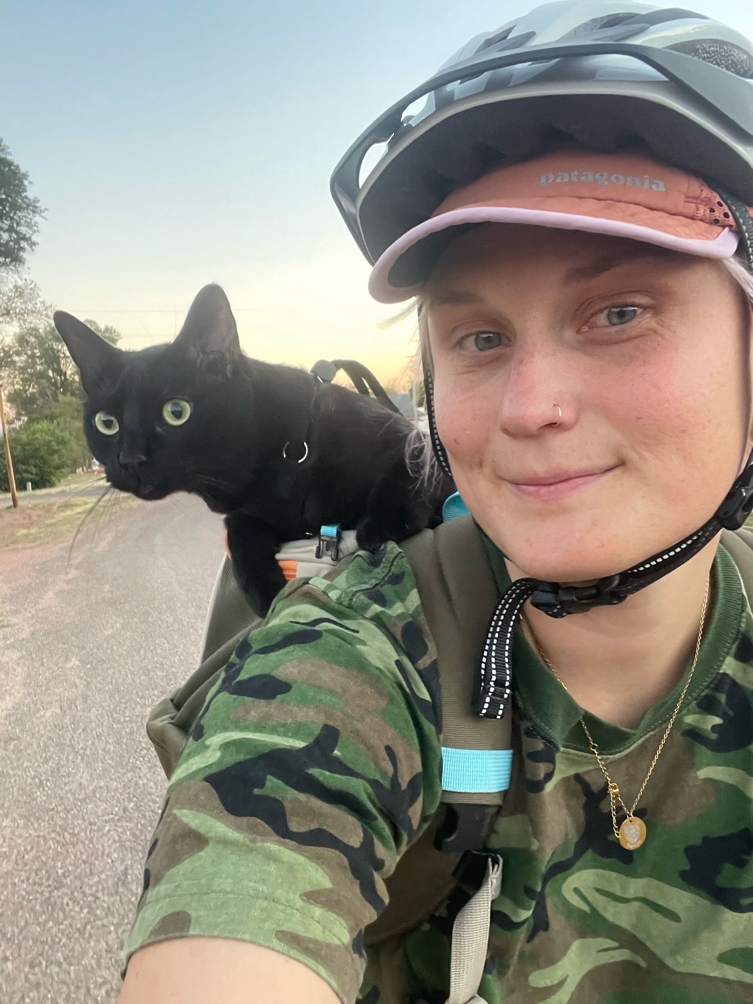 a lady with a cat on her shoulder as she rides a bike. the cat looks intruiged.