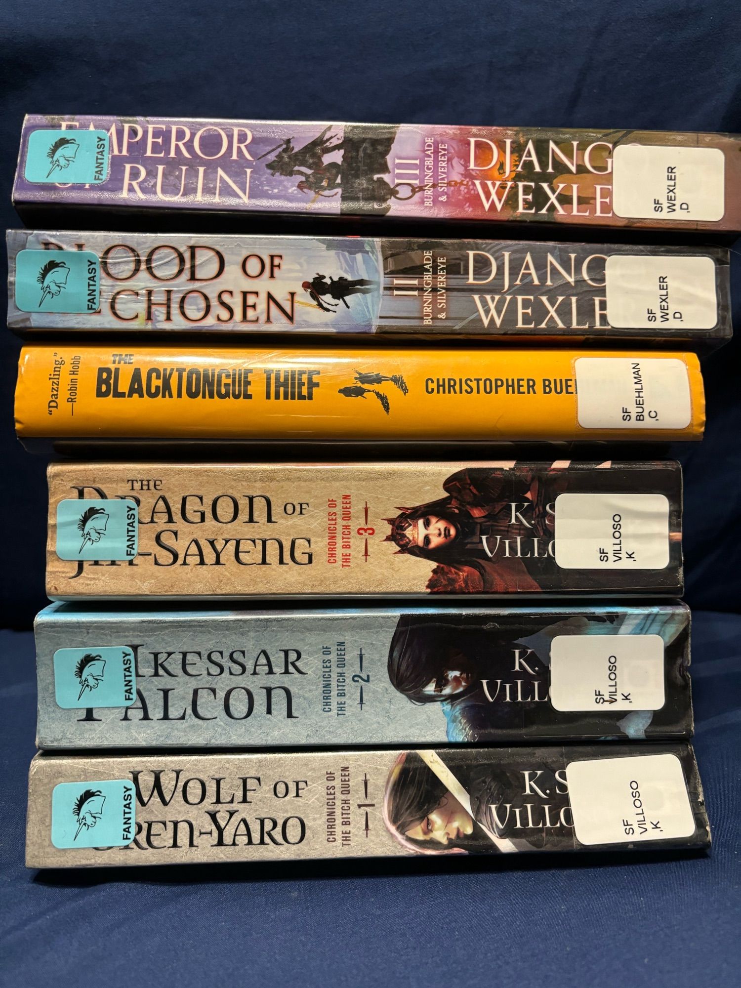 A stack of library books. Blood of the Chosen and Emperor of Ruin by Django Wexler, The Blacktongue Thief by Christopher Buehlman, The Wolf of Oren Yaro, The Ikessar Falcon and the Dragon of Jin Sayeng by KS Villoso.