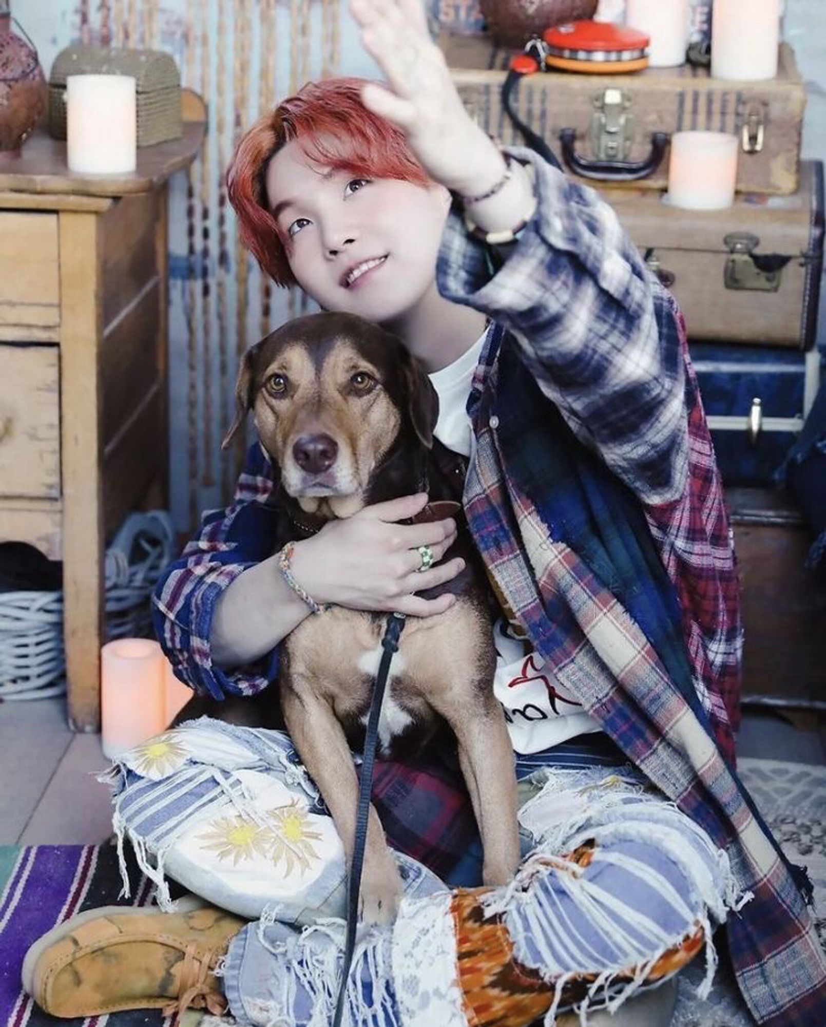 Yoongi is cuddling with a dog on his lap for a photoshoot. Yoongi’s hair is red and his outfit is intentionally rugged and colourful