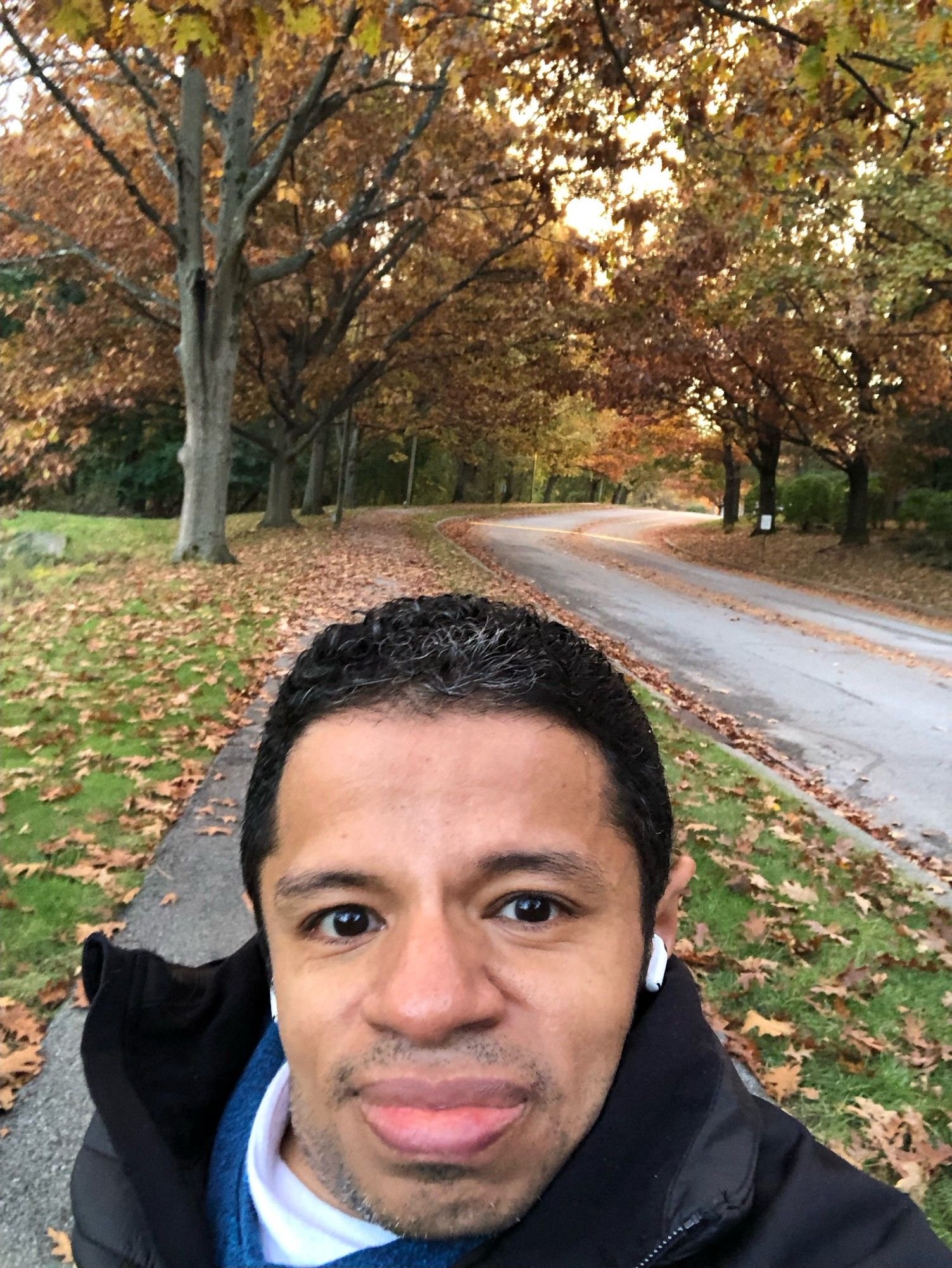 A pic of me walking on a long paved path with peak Fall foliage and tons of fallen leaves in the background.