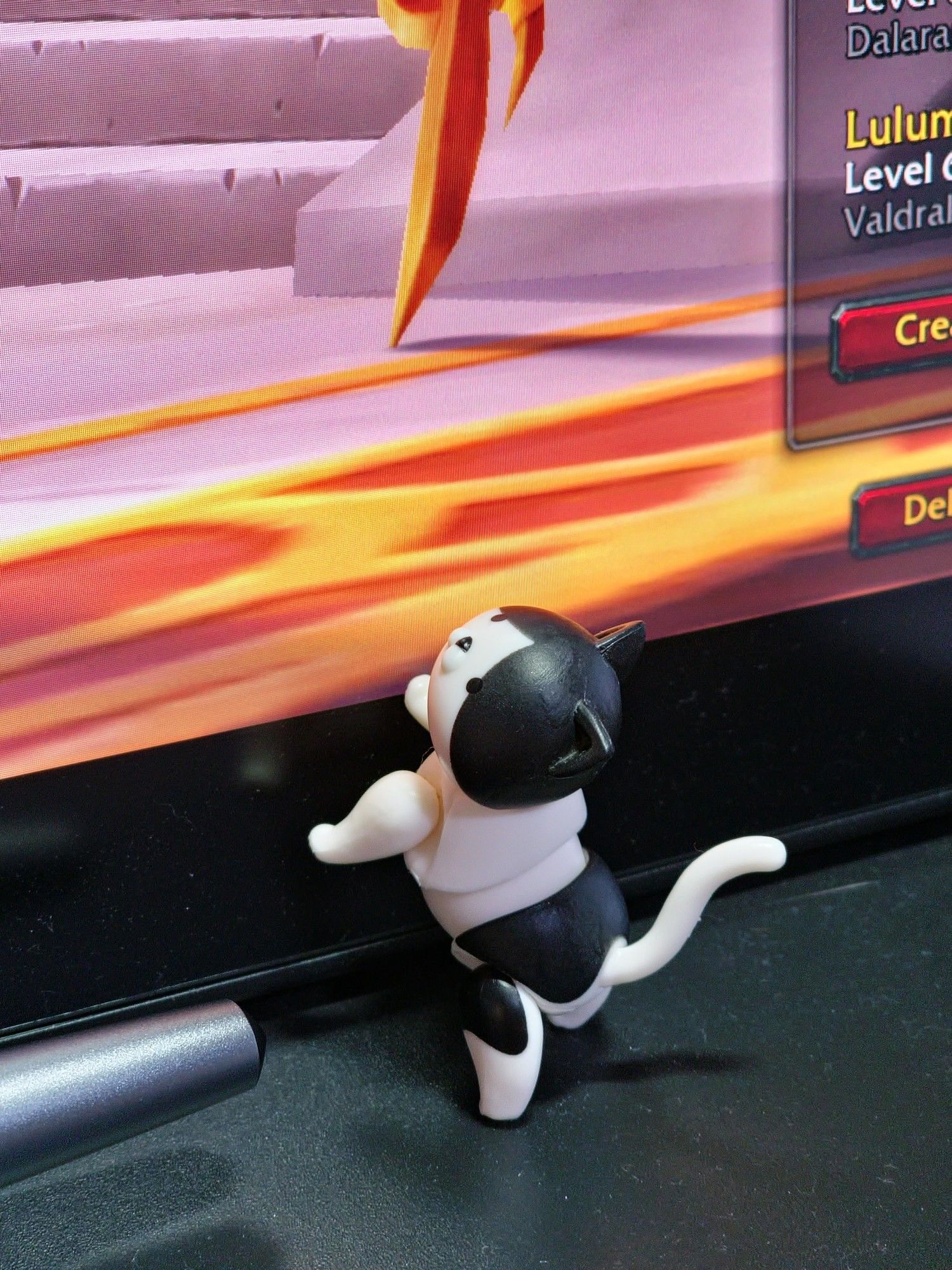 A small 1 12th scale black and white cat stretches up a computer monitor on its back paws.