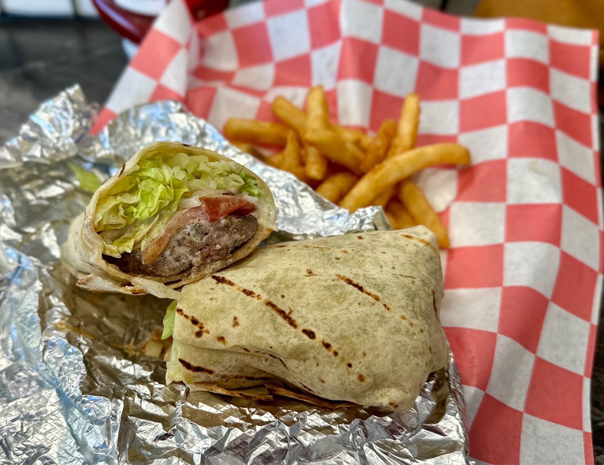 a griddled lavash bread wrap stuffed with kebab meat, lettuce, tomatoes, and sauce. comes with french fries on a checkered red wrapper