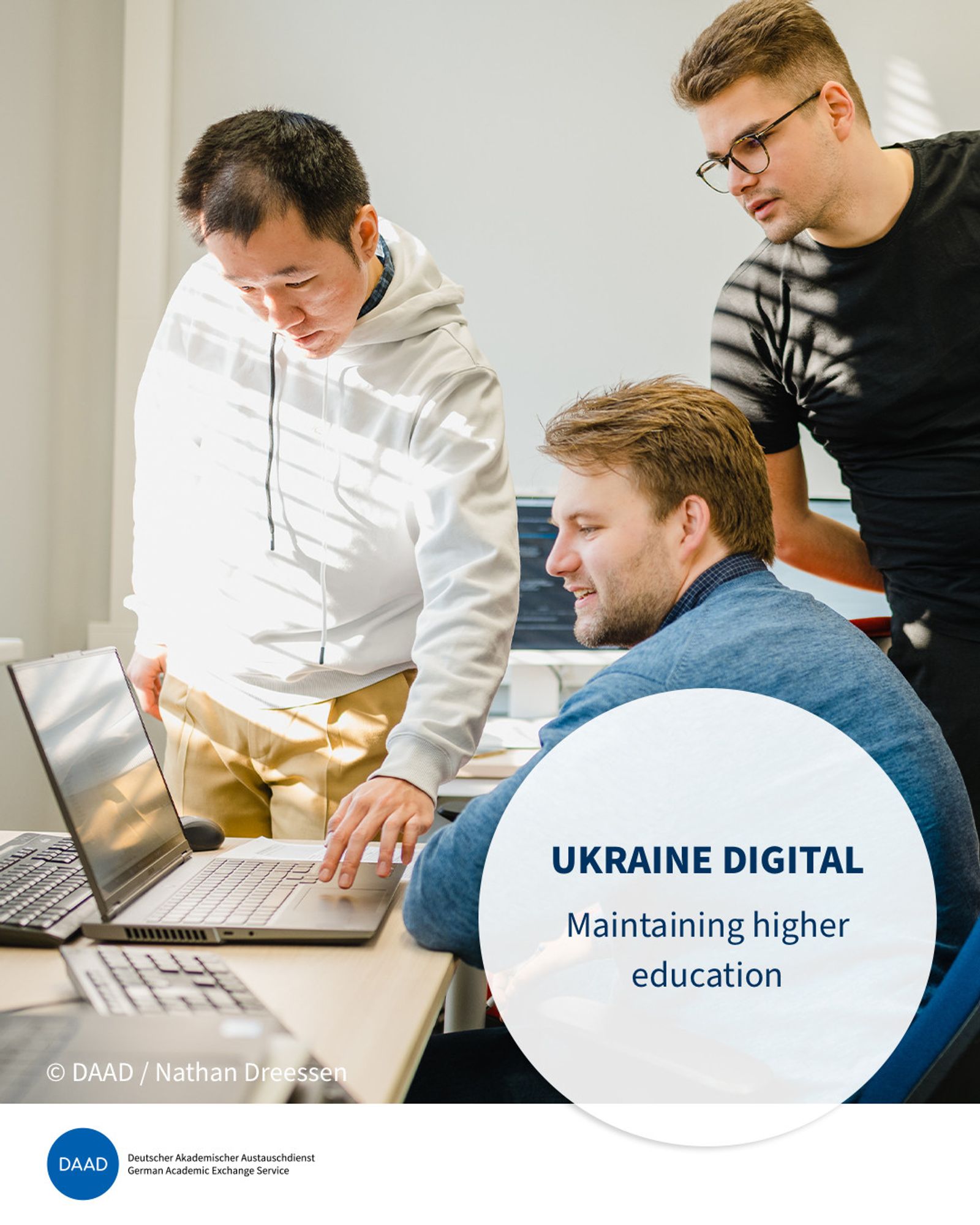 Three men in their twenties are standing and sitting around a desk, looking at a laptop together. A round eye-catcher shows the title: Ukraine digital. Maintaining higher education. Image source: DAAD, Nathan Dreessen.