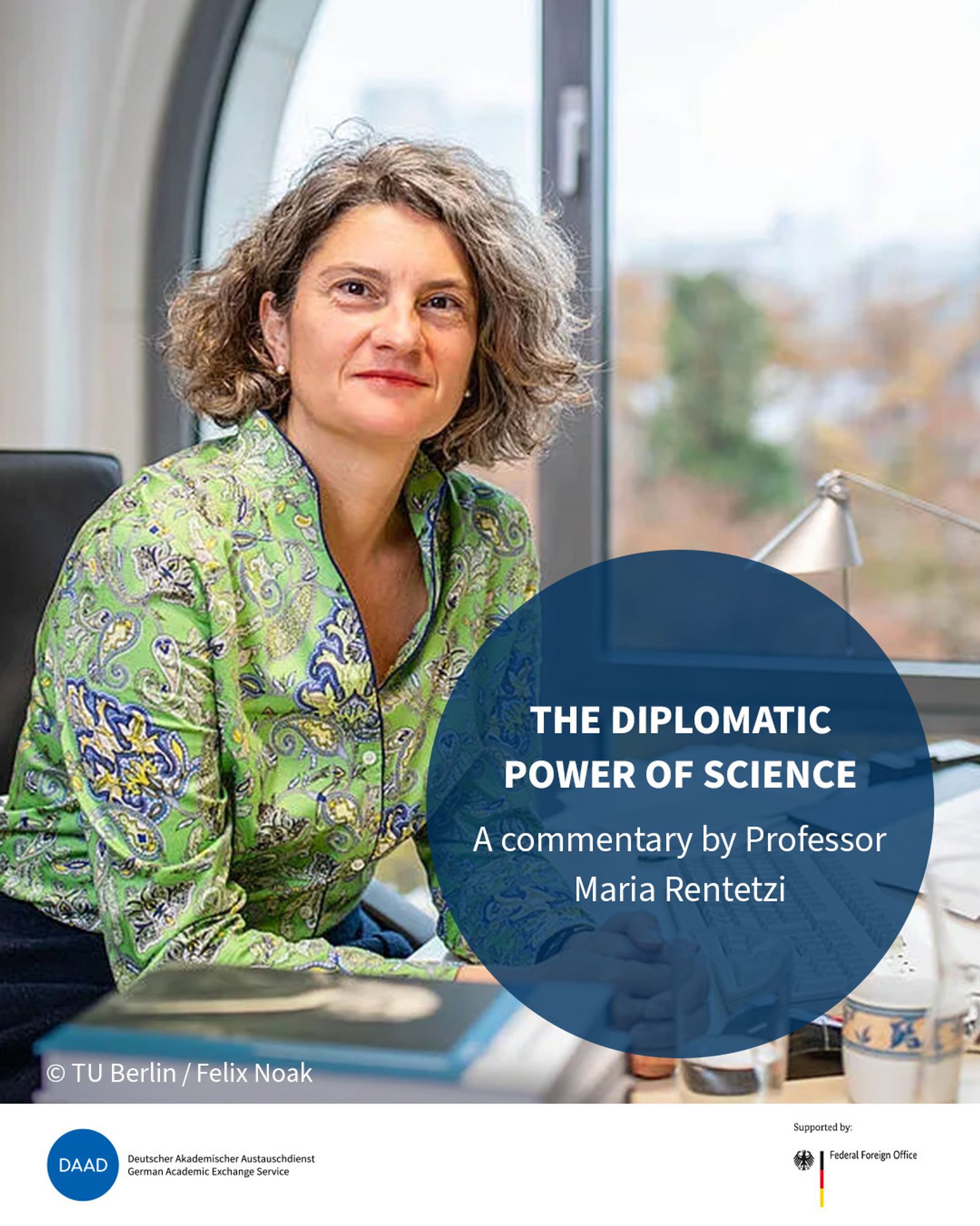 Maria Rentetzi is sitting at her desk. Her grey-blond locks are cut to her chin and she is wearing a green top. An eye catcher shows the title: The diplomatic power of science: A commentary by Professor Maria Rentetzi. Image source: André Gottschalk.