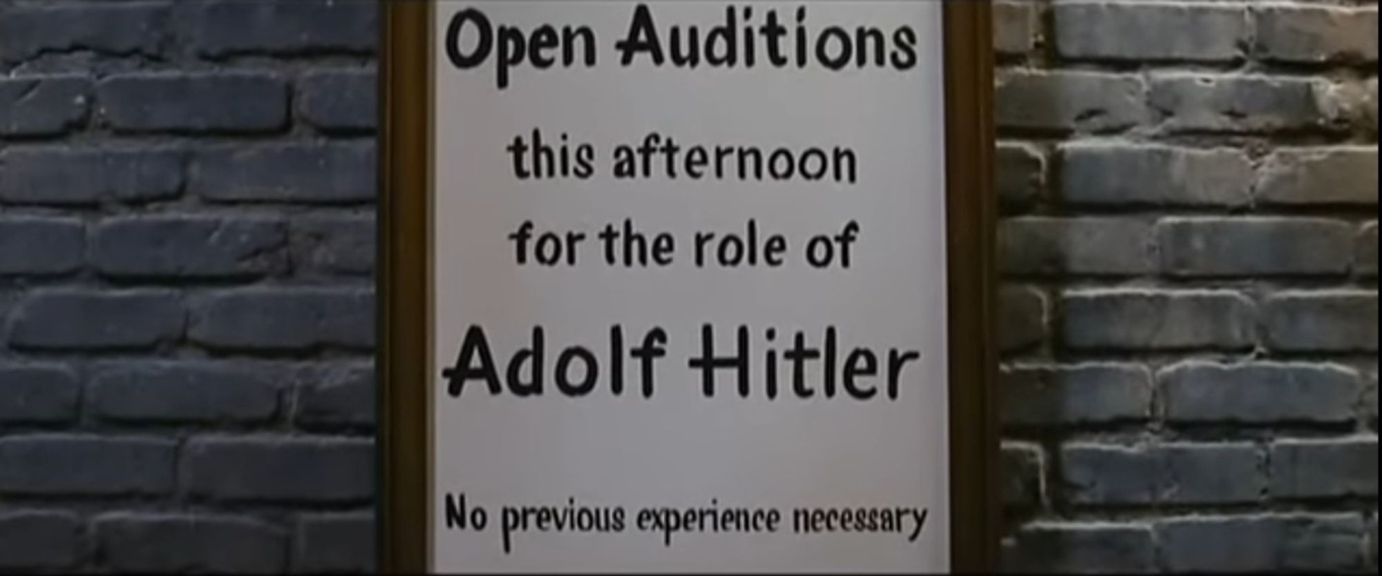 Szene aus dem Musicalfilm THE PRODUCERS von Mel Brooks: an einer Hauswand hängt ein Plakat mit der Aufschrift: "Open Auditions this afternoon for the role of Adolf Hitler. No previous experience necessary."