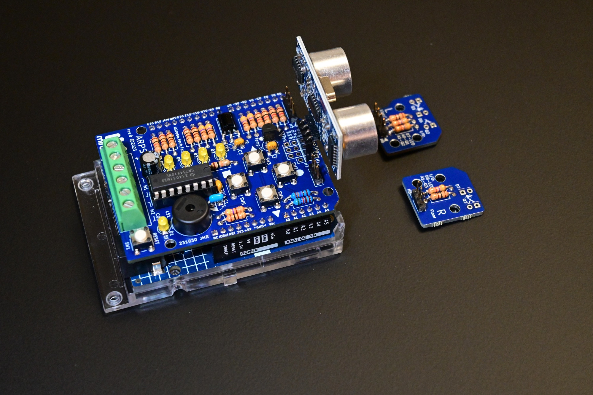 An ARPS circuit attached to an Arduino UNO. ARPS includes four pushbuttons, four LEDs, a piezo speaker, a temperature sensor, an IR demodulator, a motor driver IC, and two break-away optical floor sensor modules (right). Digital I/O expansion pins at the right side of ARPS can hold a SONAR module.