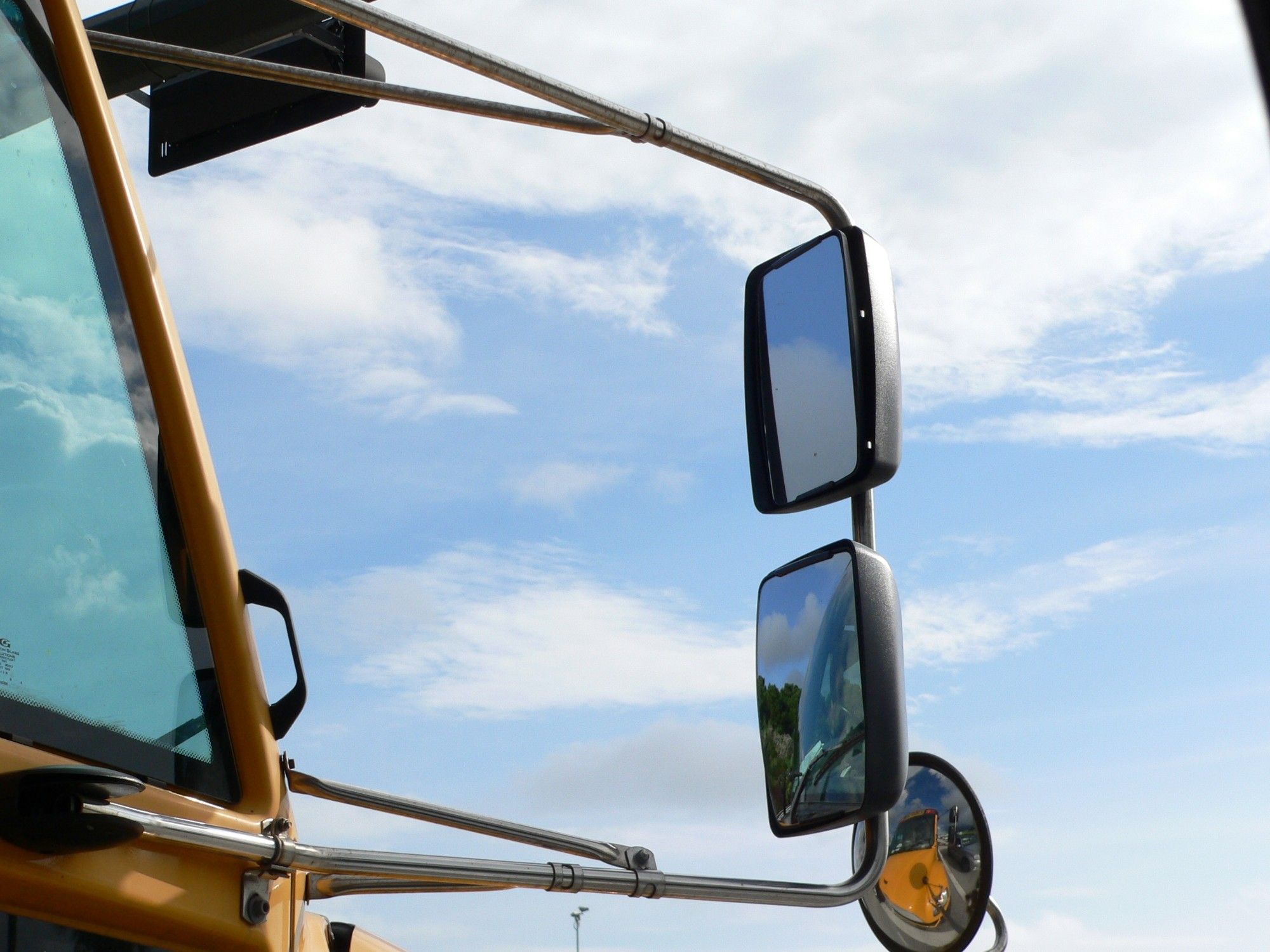 The right-hand mirror and support on a yellow schoolbus - lit by morning sun, and framed against the Florida sky