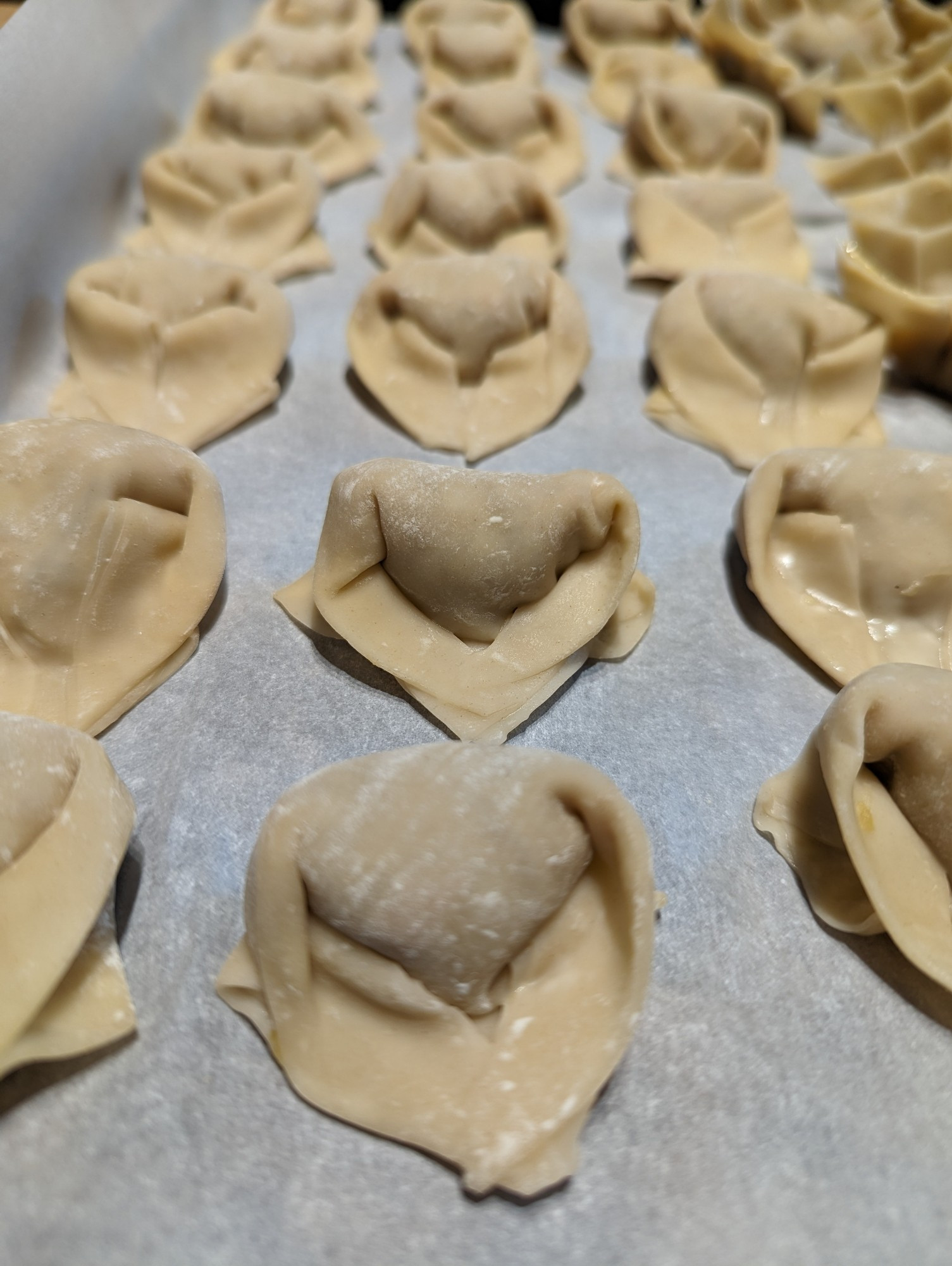 Handfolded wontons on a baking sheet tray