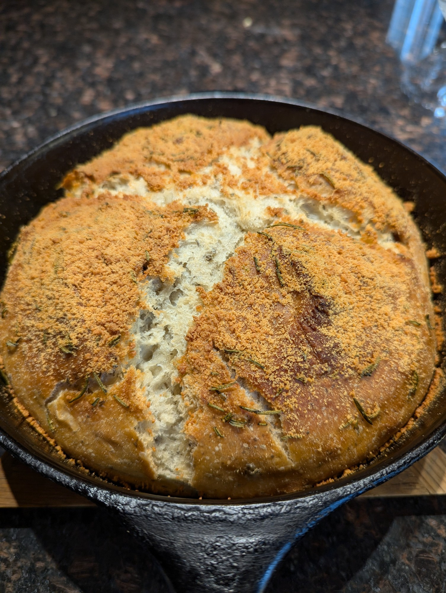 Iron skillet still warm from the oven filled with a golden brown loaf of bread slashed with an x for more crispy bites 