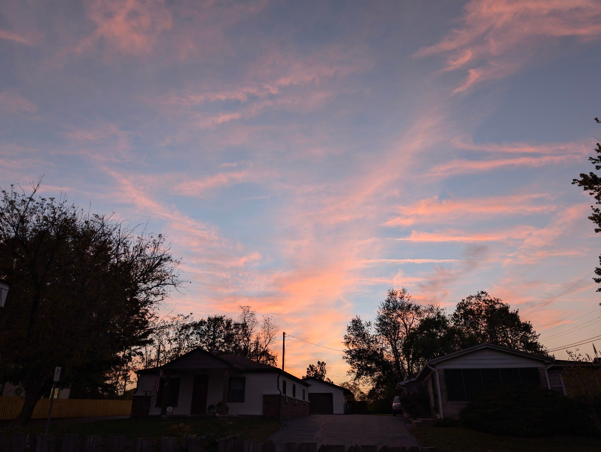 A sunset over a few houses in the foreground. The sky is a light blue gradient with pink clouds. 