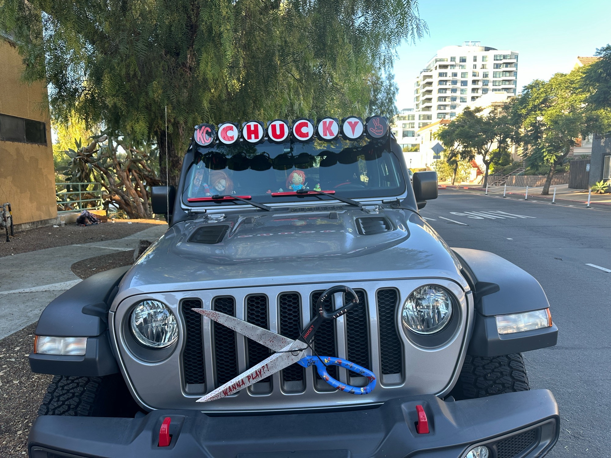 Front view of a Jeep with CHUCKY spelled across the front windshield and a giant pair of scissors on the grill emblazoned with “Wanna play?” Multiple Chucky toys can be seen inside the cab of the Jeep.