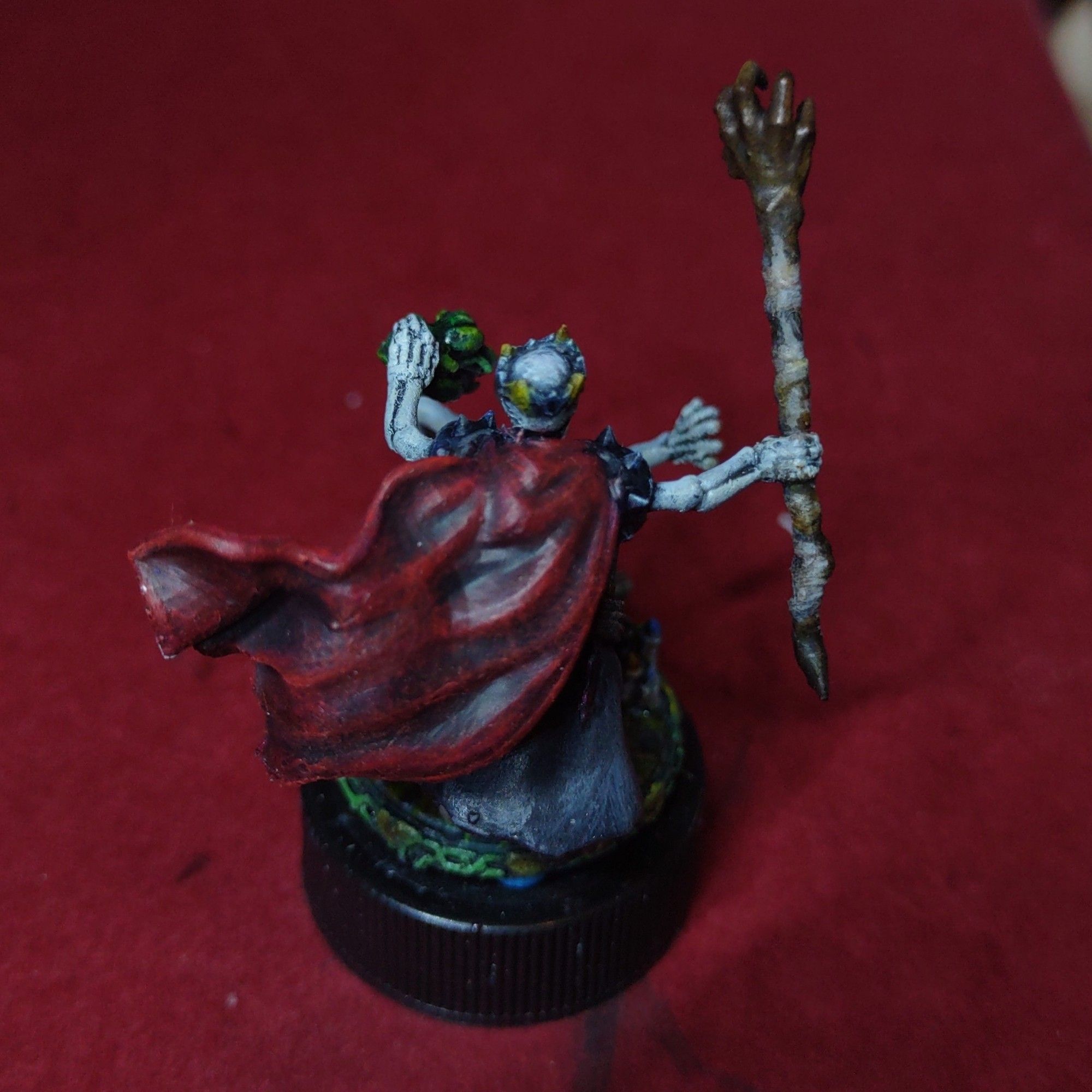 A miniature of a lich holding a claw shaped staff, candles on the ground, and a spell effect summoning a skeleton