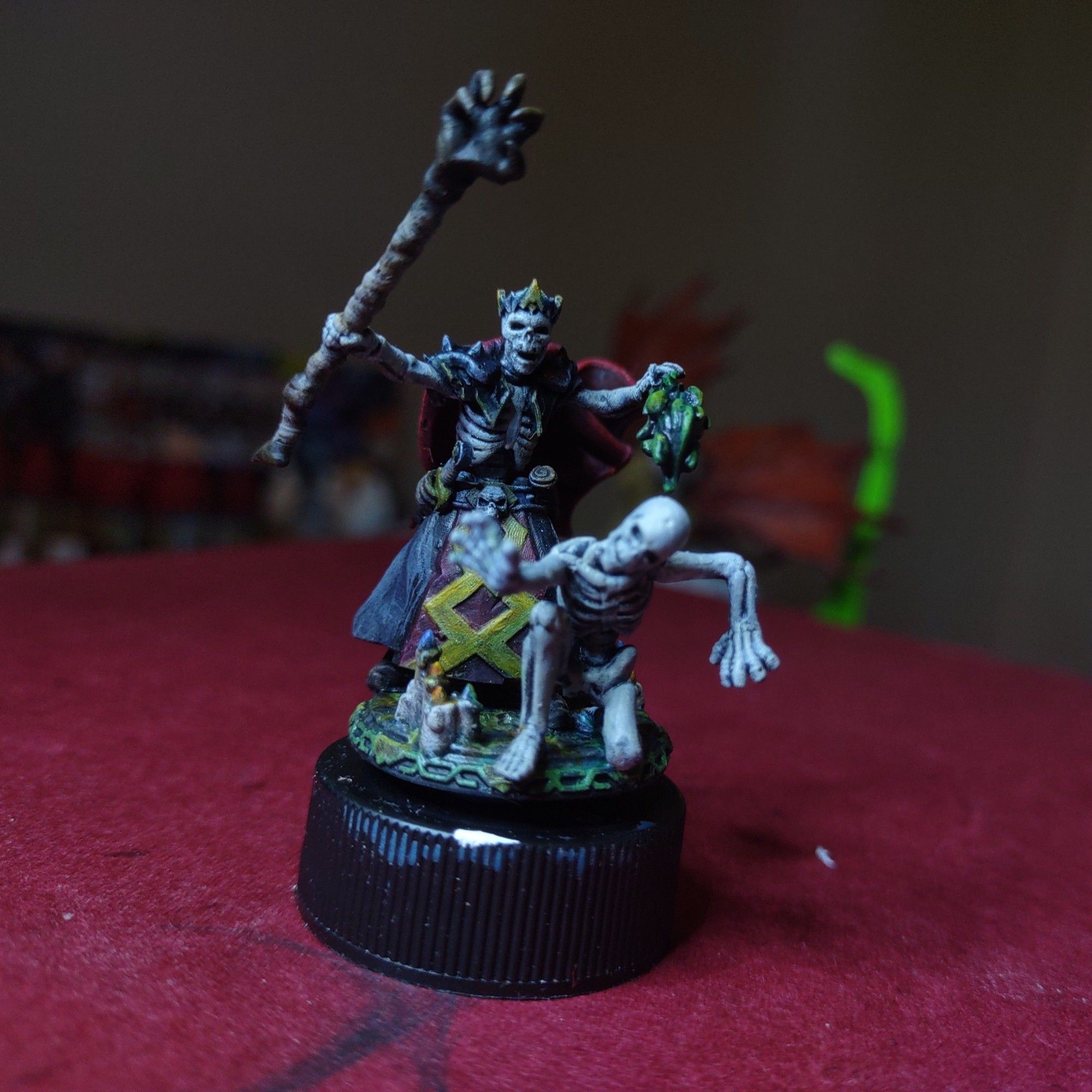 A miniature of a lich holding a claw shaped staff, candles on the ground, and a spell effect summoning a skeleton