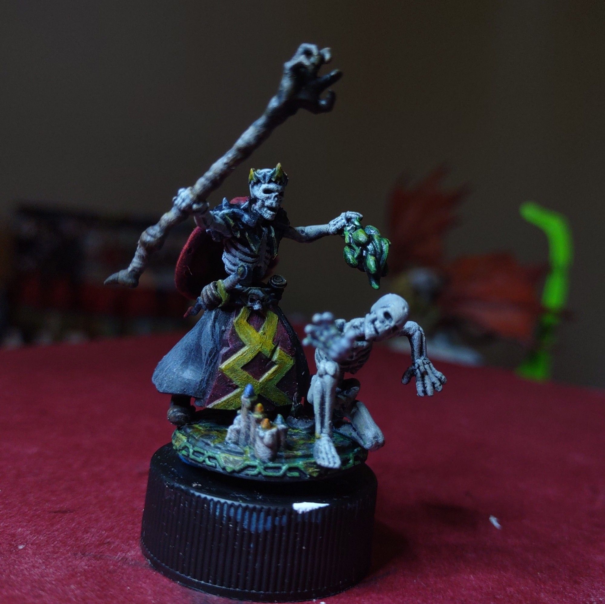 A miniature of a lich holding a claw shaped staff, candles on the ground, and a spell effect summoning a skeleton