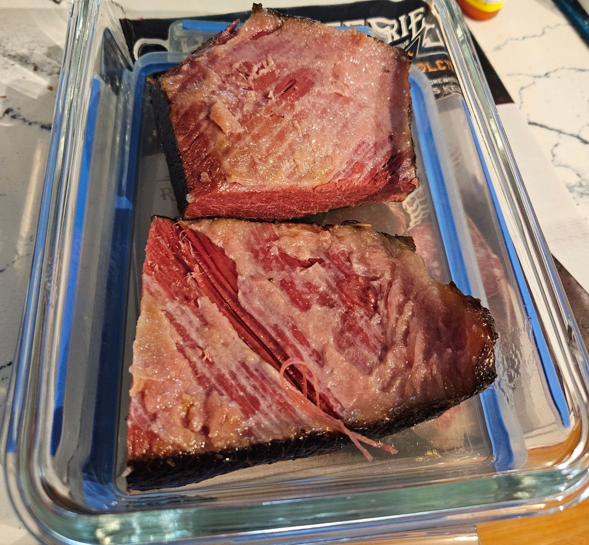 Well cured brisket in two pieces, placed in a glass dish, atop a book called Charcuterie.