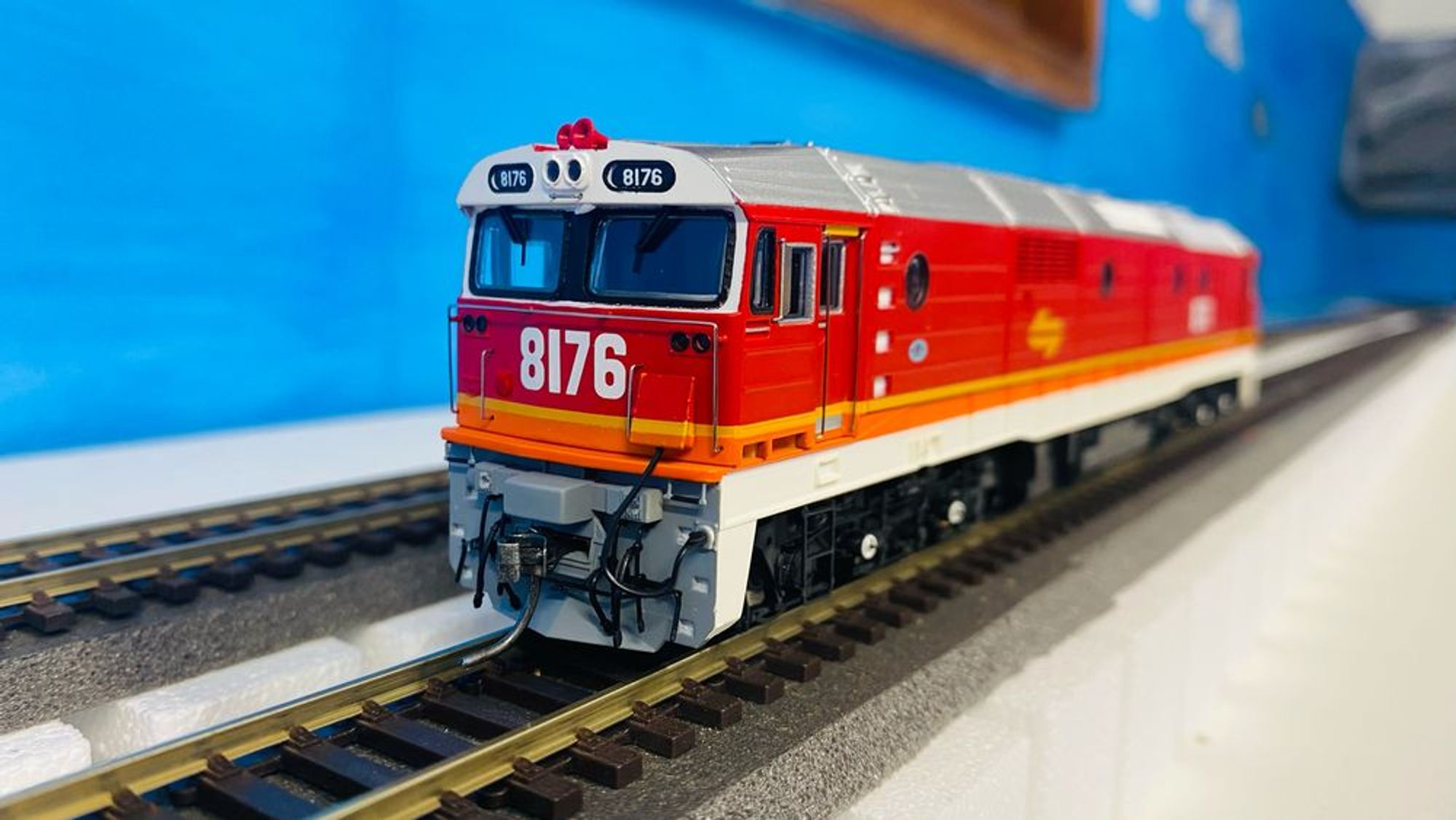 Picture of a model train locomotive, red with orange and yellow stripes and a silver roof, and the number 8176