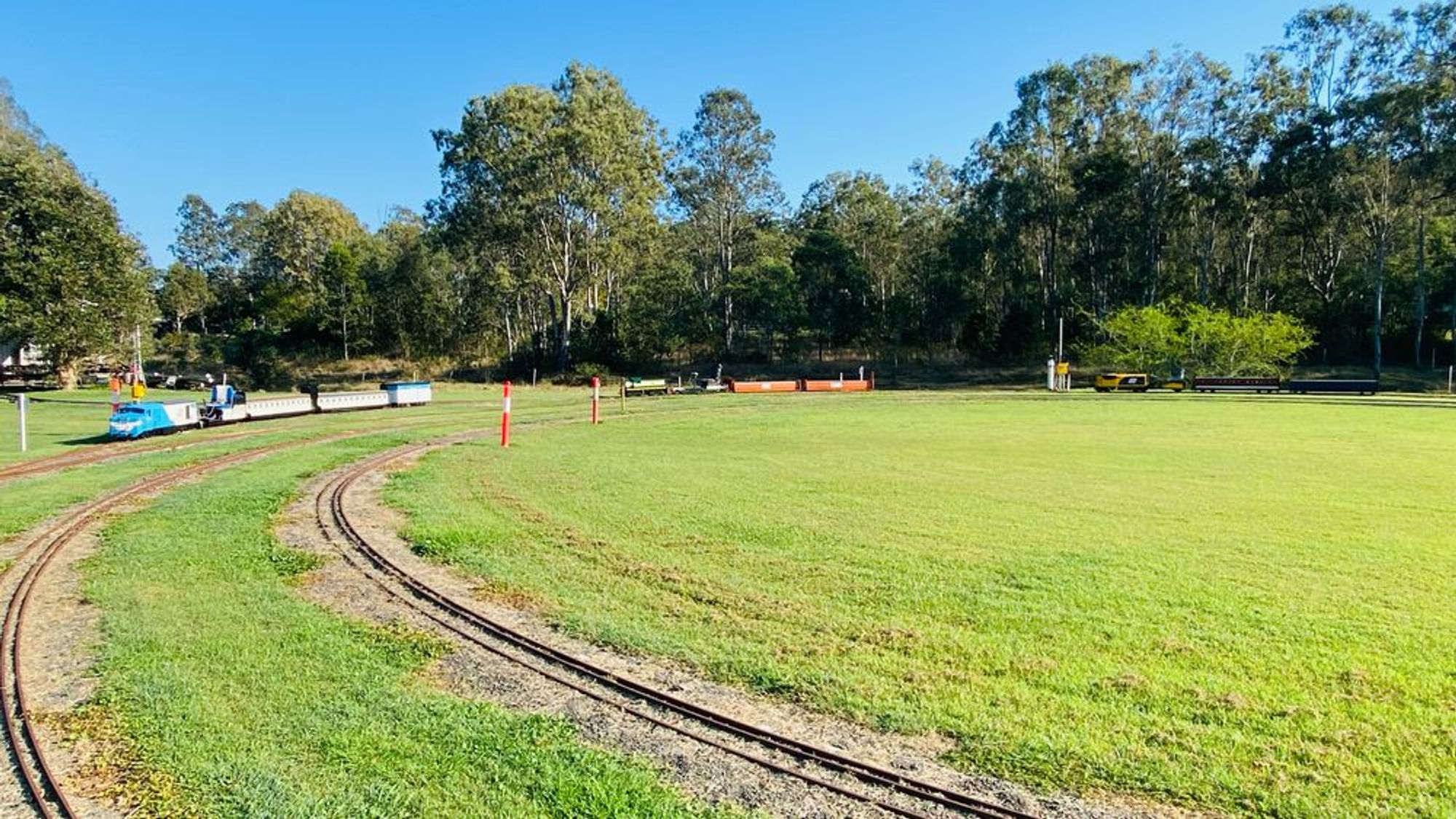 Ride-on model trains lined up on a track, surrounded by grass and with trees in the background