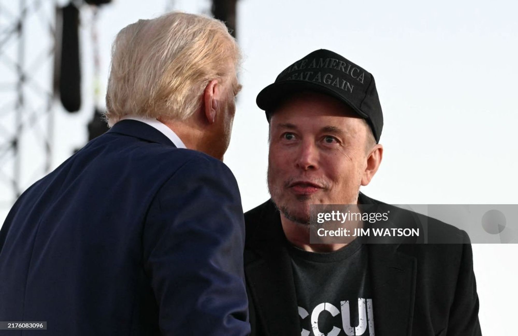 Donald Trump speaking closely to Elon Musk, who looks high on rave drugs. Image via Getty, photographer Jim Watson