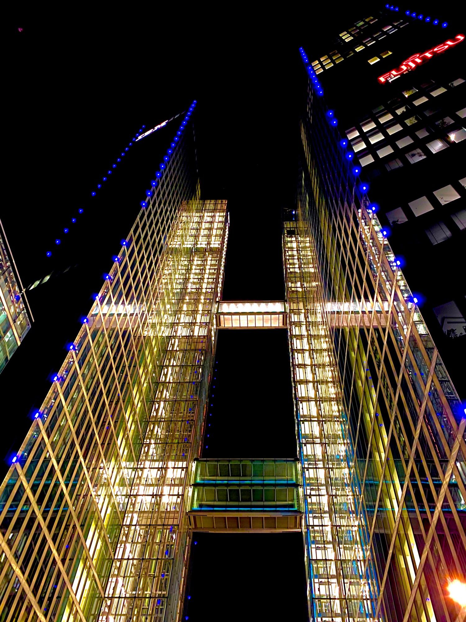 Gläserne Hausfassade bei Nacht in Schwabing. 
2 Gebäudeteile sind mit gläsernen Übergängen miteinander verbunden. 
Ein paar bunte Leuchten sind auch mit dabei.