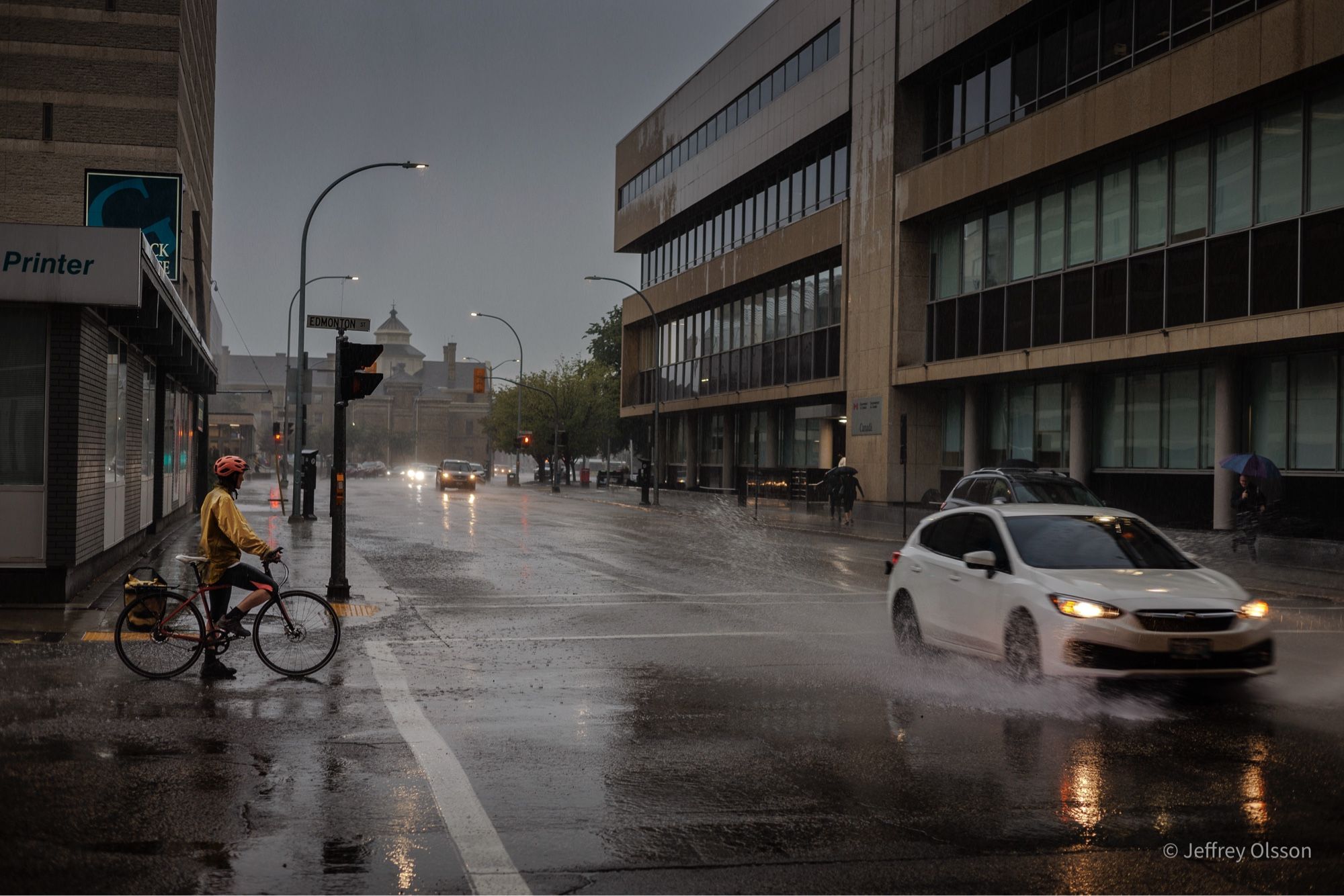 A cyclist waits for cars splashing through water before going through intersection.