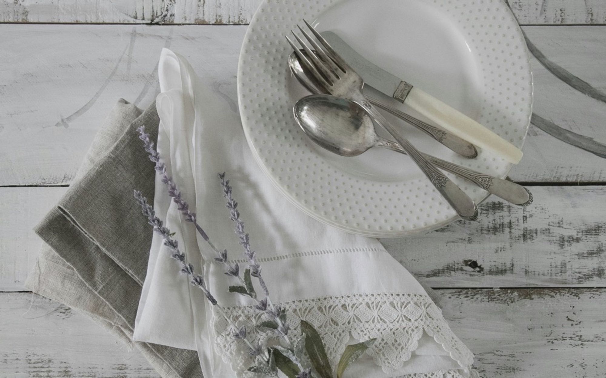 A photo of a white plate, napkins, and cutlery on a white wooden table. From Unsplash