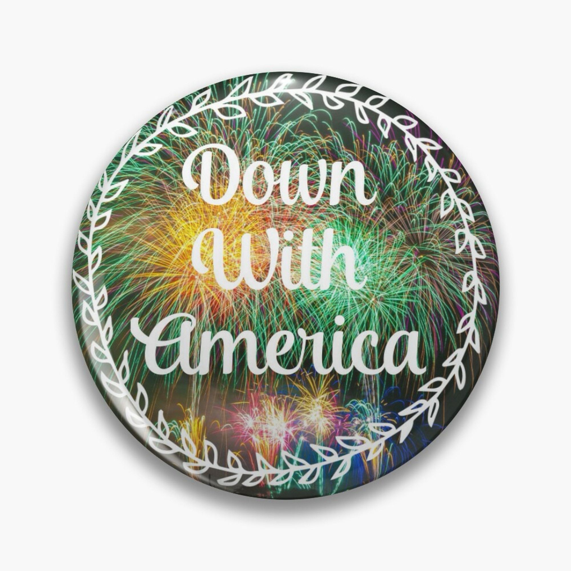 An enamel pin with fireworks in the background. At the forefront, there’s a white floral ring around the edge of the pin. In the middle, in white fancy cursive text, it reads ‘Down With America’