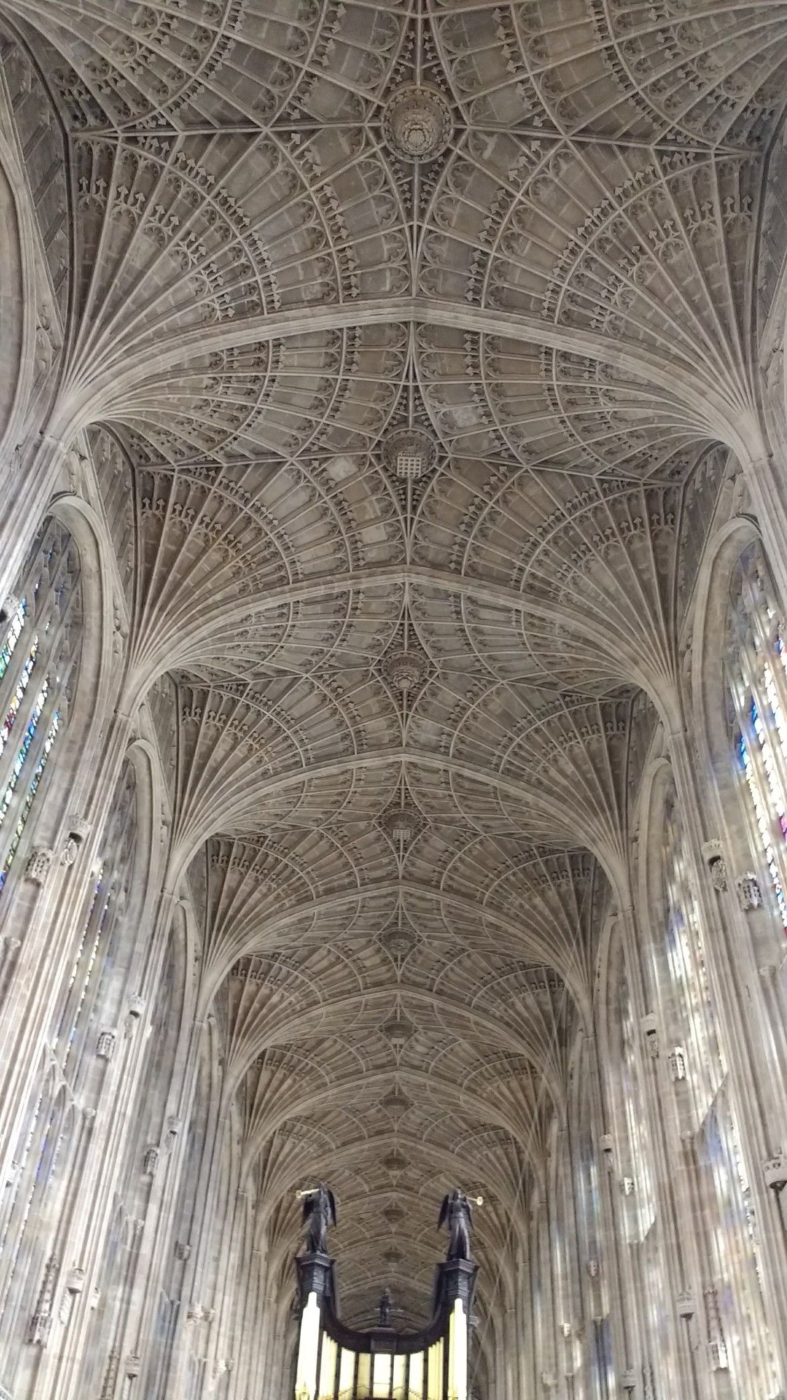 To the left and right, tall arched stained glass windows and overhead, stretching into the distance, the arched and vaulted ceiling in intricately carved stonework. The pipes of the organ are visible at the far end.