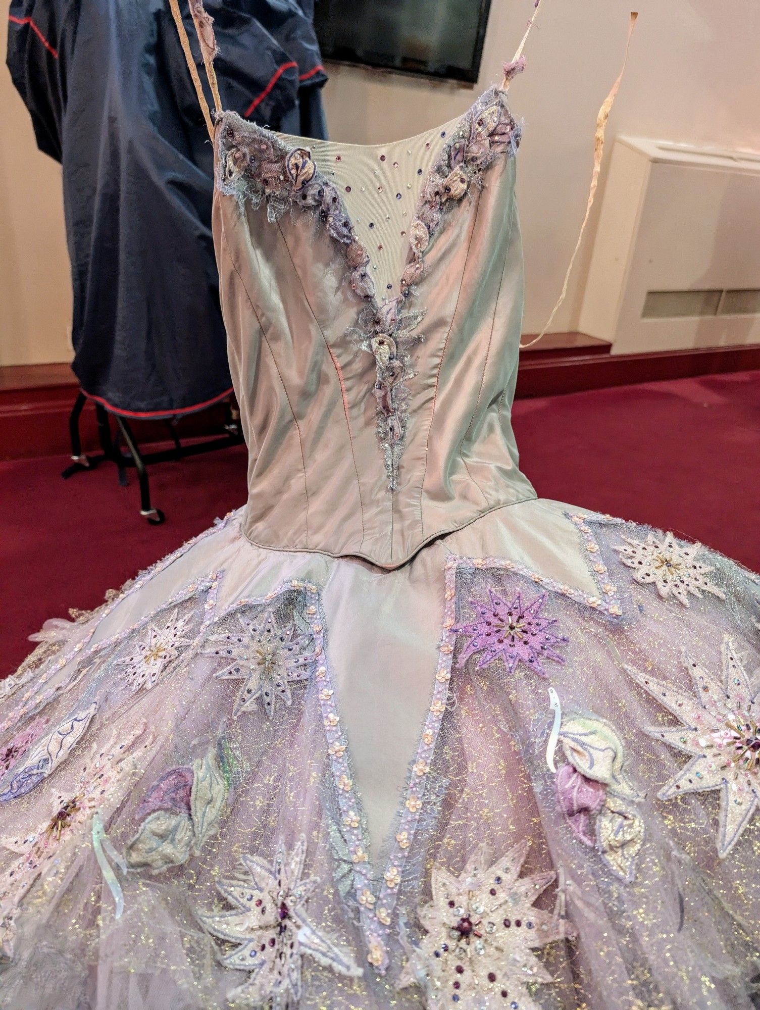 A ballet tutu in shades of lilac with satin bodice and radiating points on the skirt with sequin covered appliquéd flower motifs on a glittery tulle background.