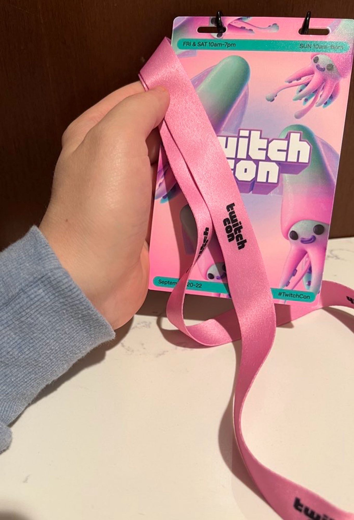 Badboyhalos tall hand holding a twitchcon badge while he dismays over the pink lanyard