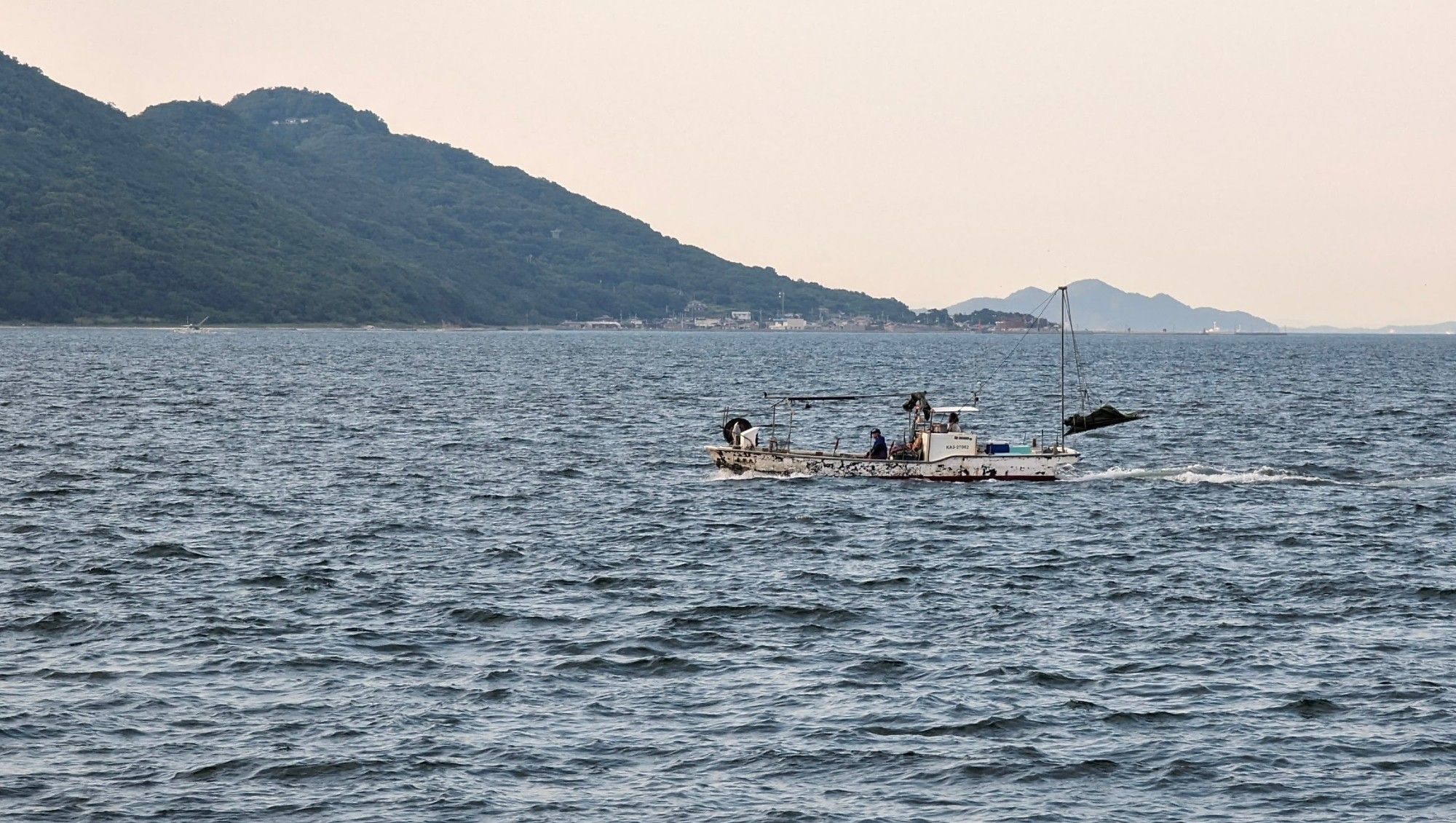 A small fishing boat navigating on the Seto Inland Sea, with Megijima in the background.