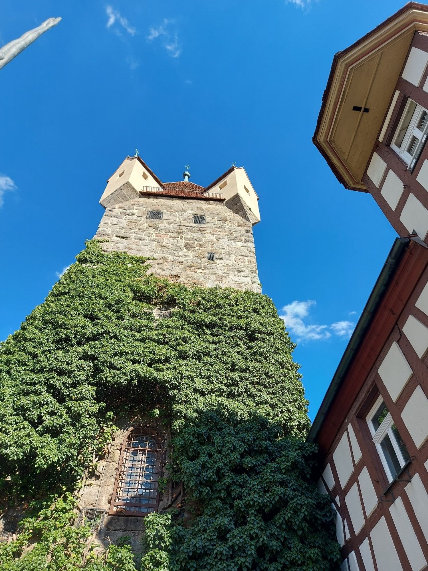 Looking up at an old stone tower, partially covered with ivy, next to a half-timbered house.