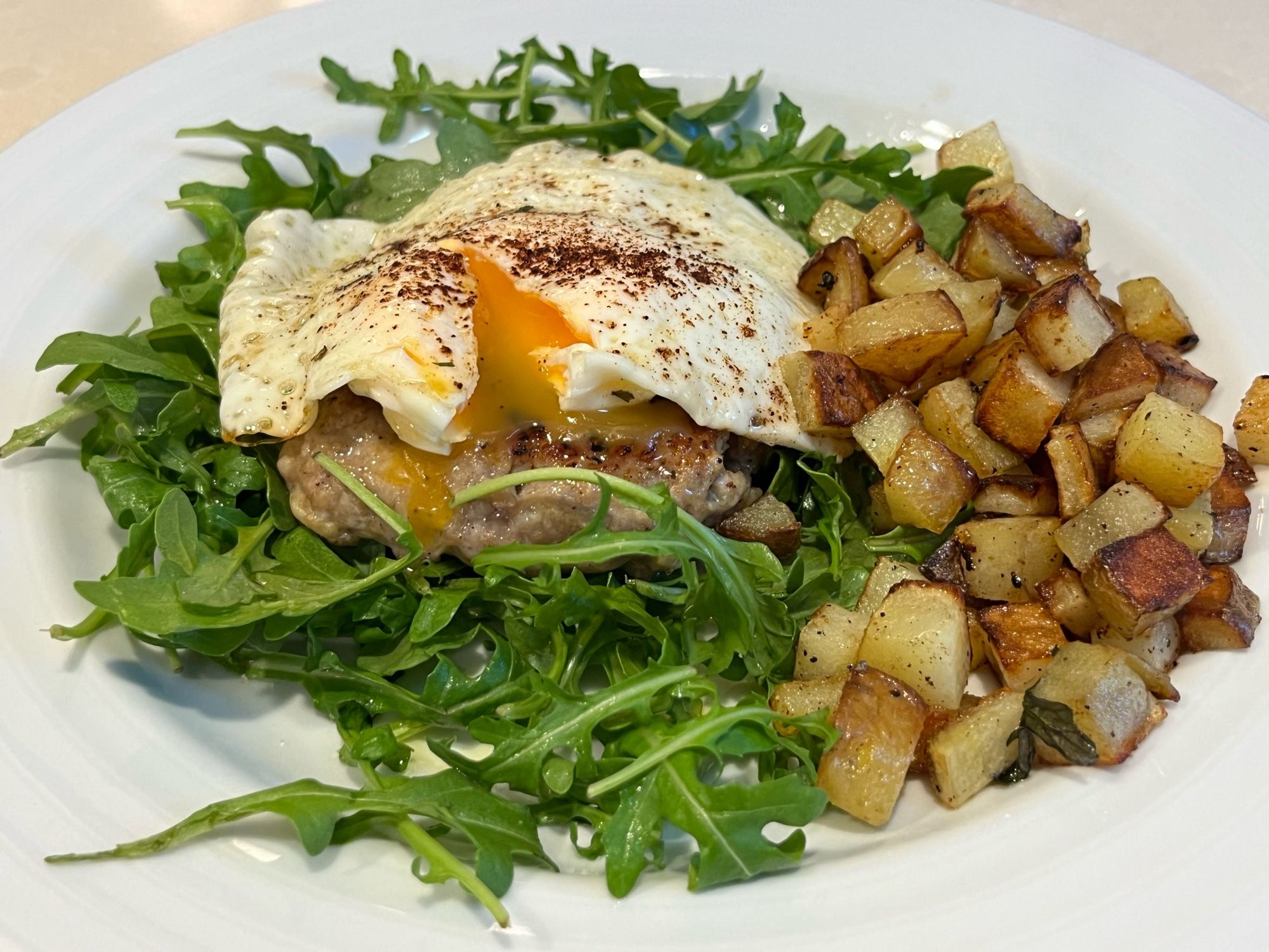 Egg over easy, slightly runny yolk. Sausage patty, on a bed of arugula with home fries on the side.