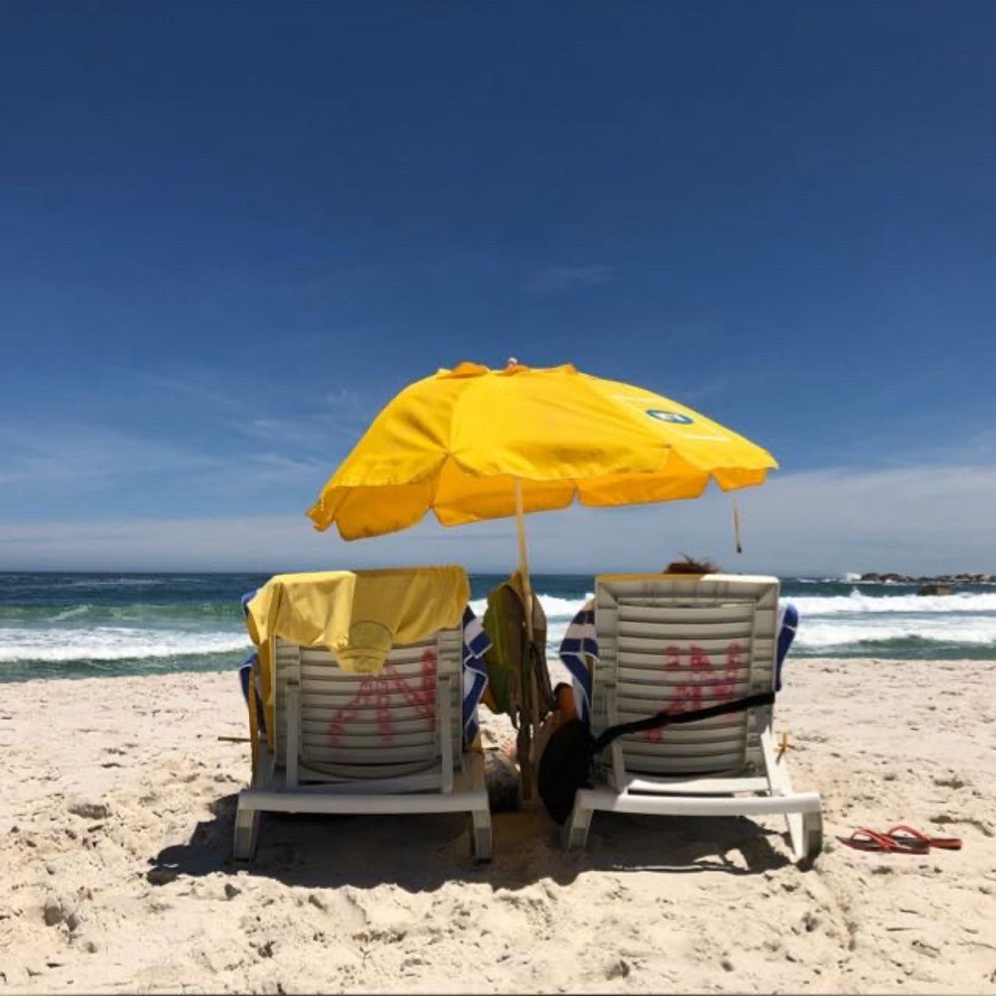 Ein gelber Sonnenschirm und zwei weiße Liegestühle am Strand