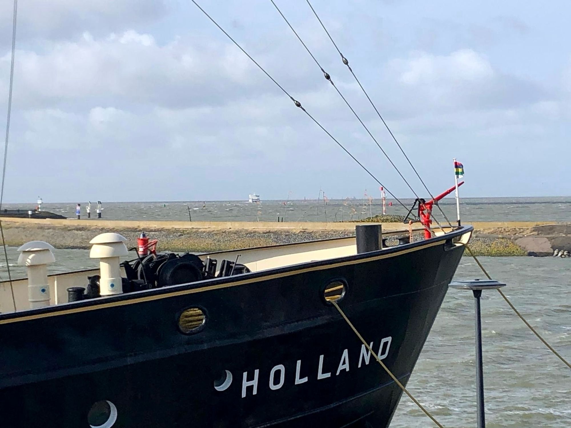 Ein Schiff mit Namen HOLLAND liegt an einem Kai vertäut. Im Hintergrund ist das Meer zu sehen