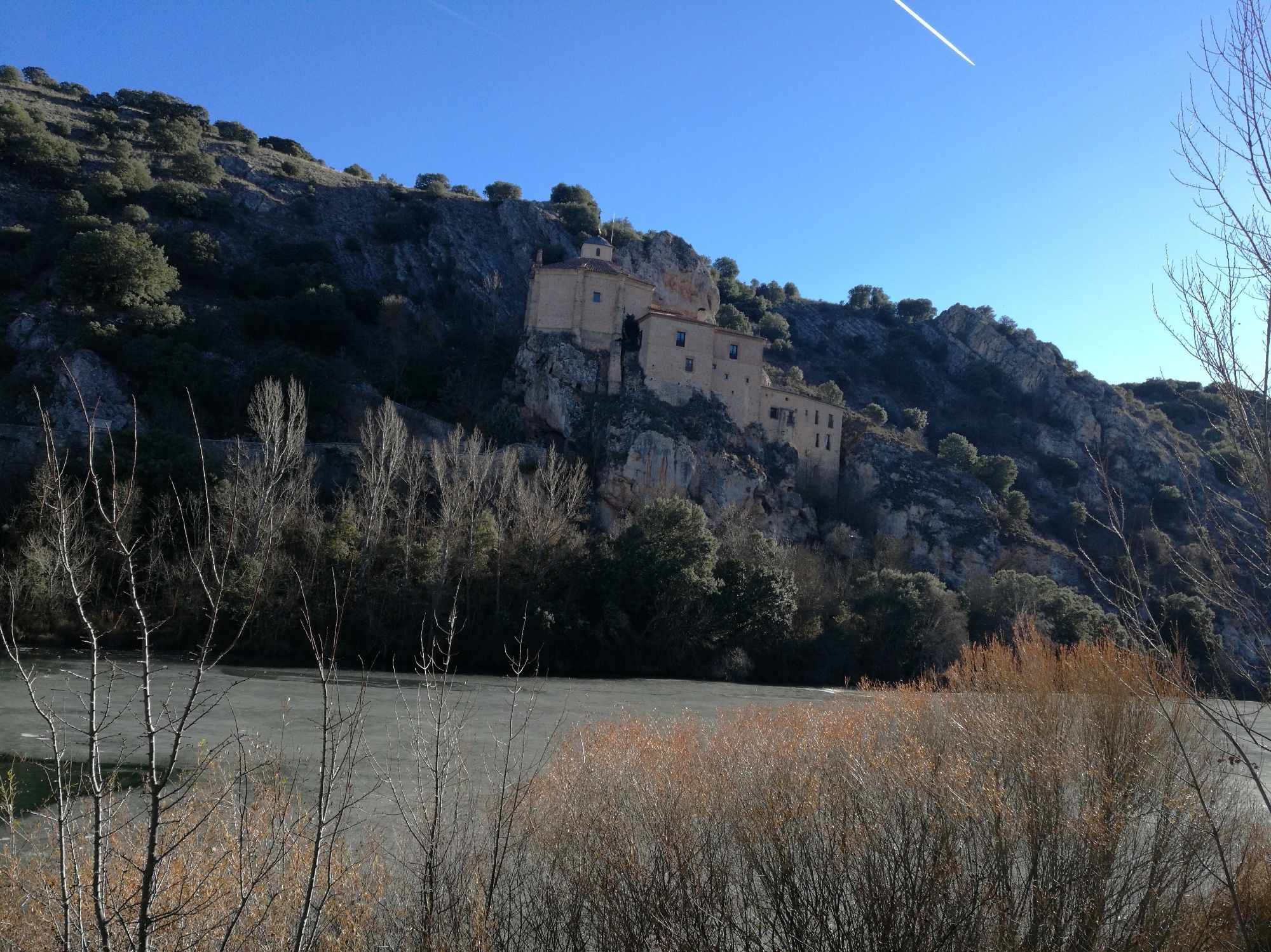 Vista de la ermita de San Saturio desde el otro lado del río, con el Duero helado en un día de invierno de cielo azul.