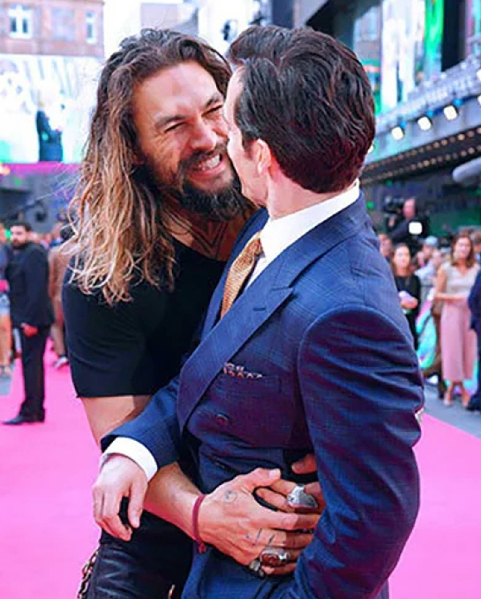 A picture of Jason Momoa smiling/hugging Henry Cavill at an event.