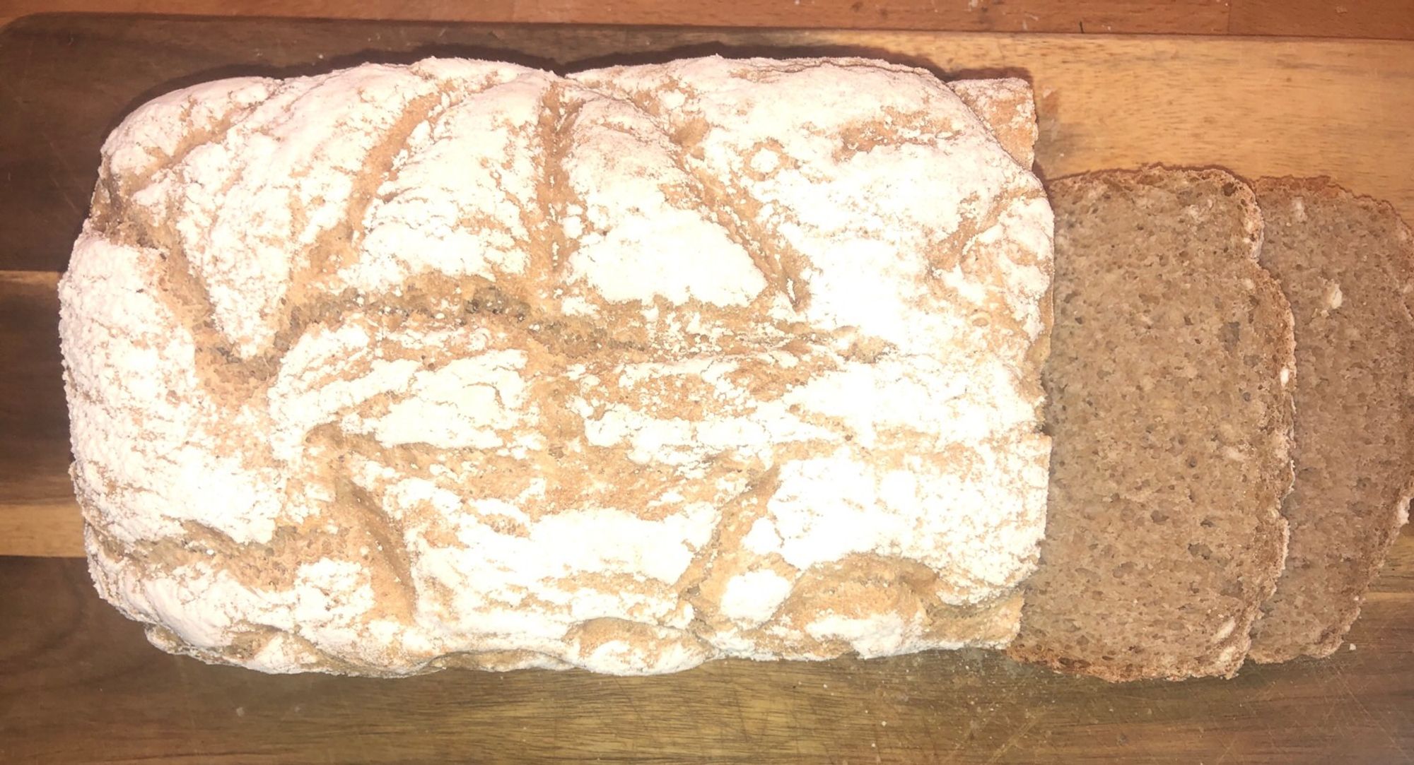 Weizenbrot in Kastenform auf einem Holzbrett. Bestreut mit Mehl. In das Brot ist ein Segelboot auf dem Wasser geritzt.