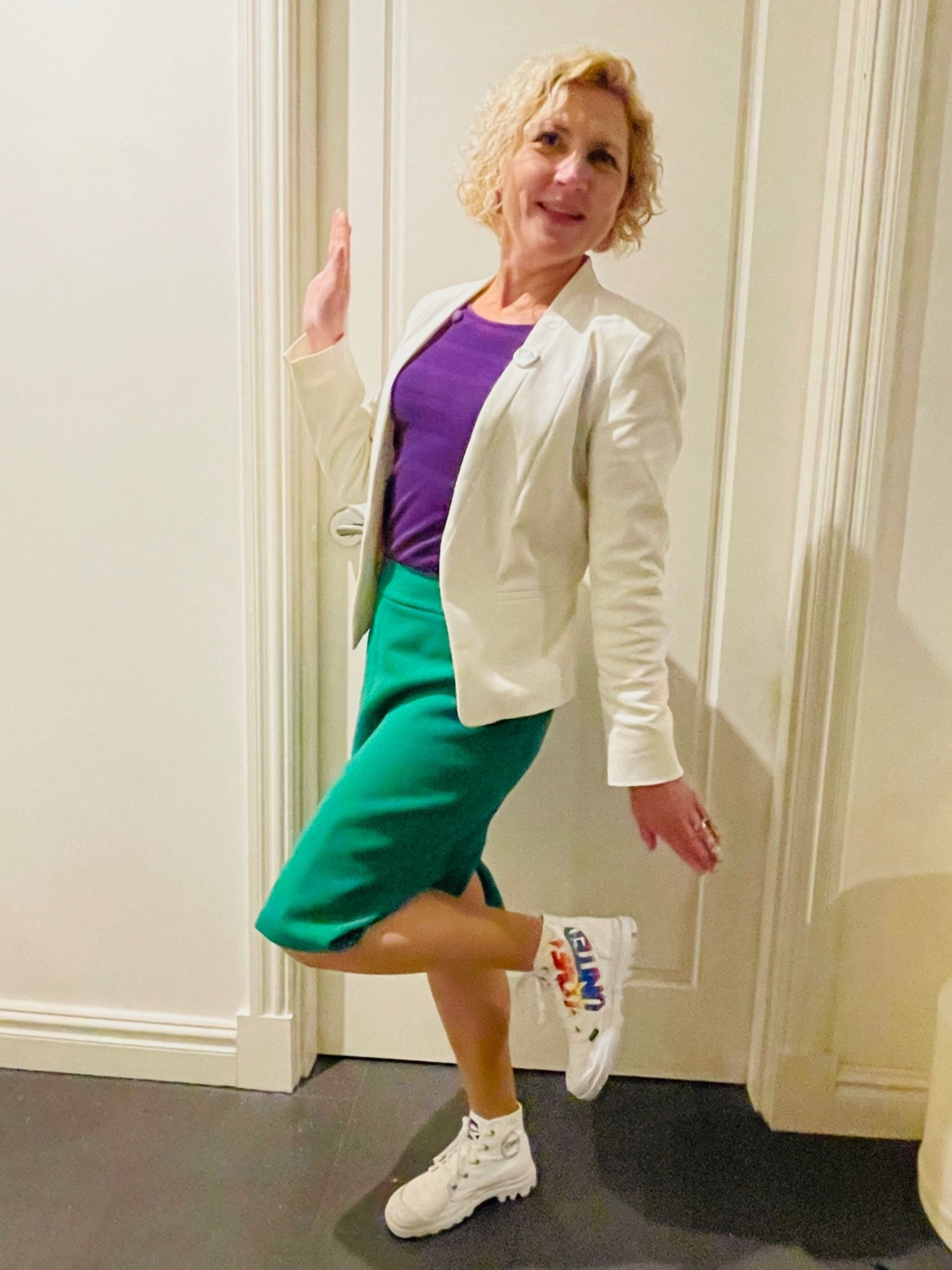 Emma wearing a white jacket, bright purple top, bright green skirt, and white hi-top sneakers with “Love United” in rainbow text on the side of the shoes.