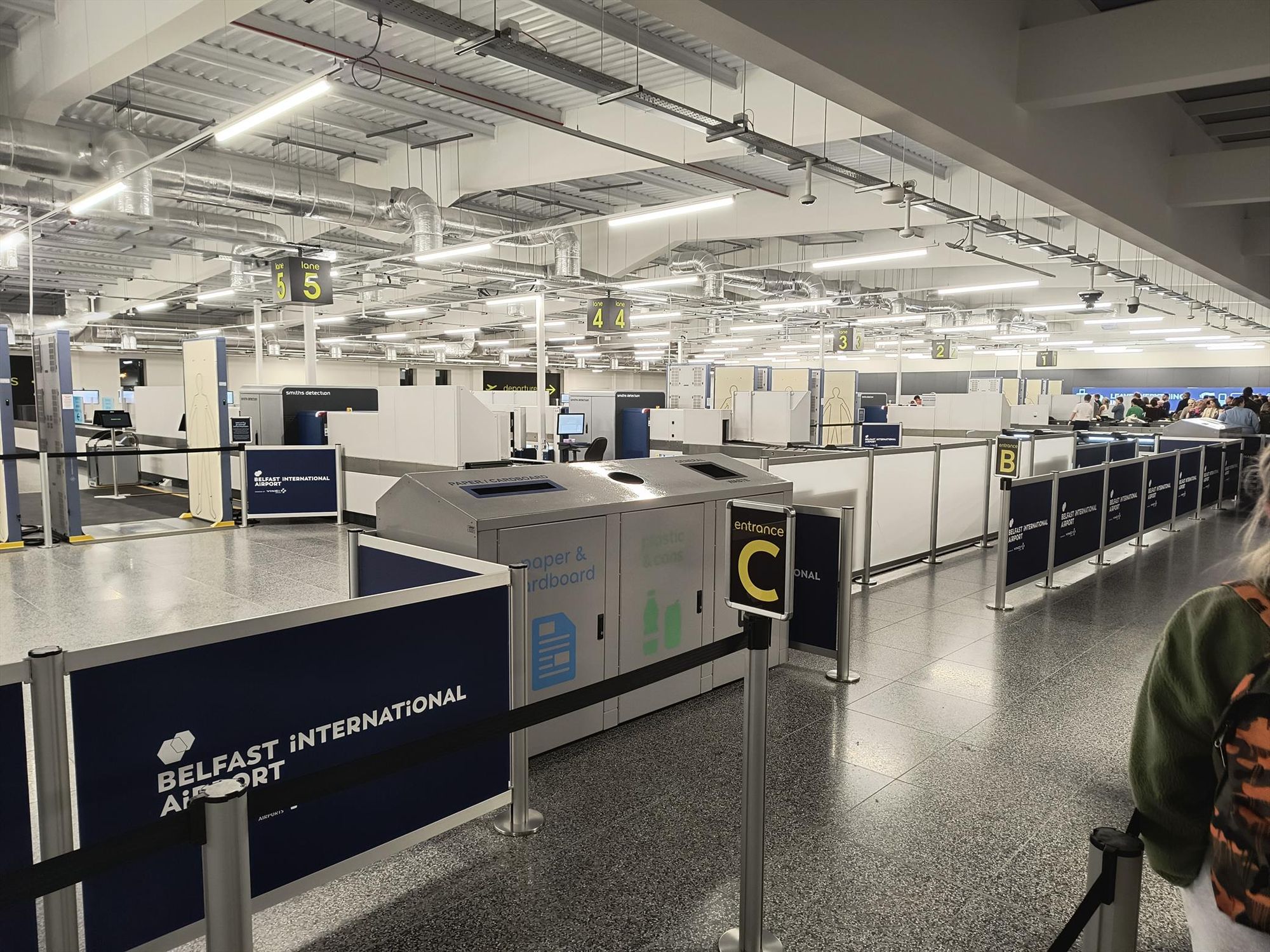 A photo of the security check at Belfast International Airport. Of the 6 available lanes, 5 are unused.