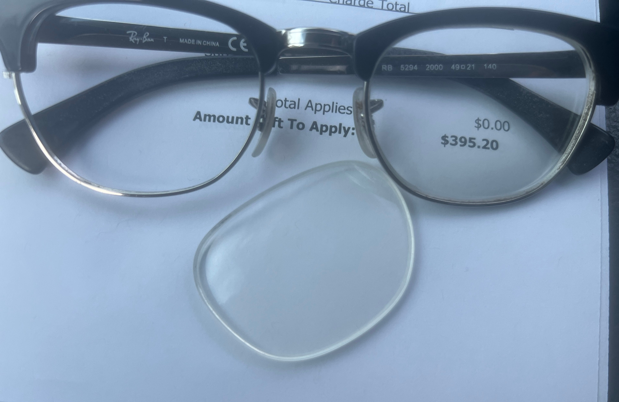 A broken pair of glasses one lens popped out sitting on a $395.20 bill for new glasses