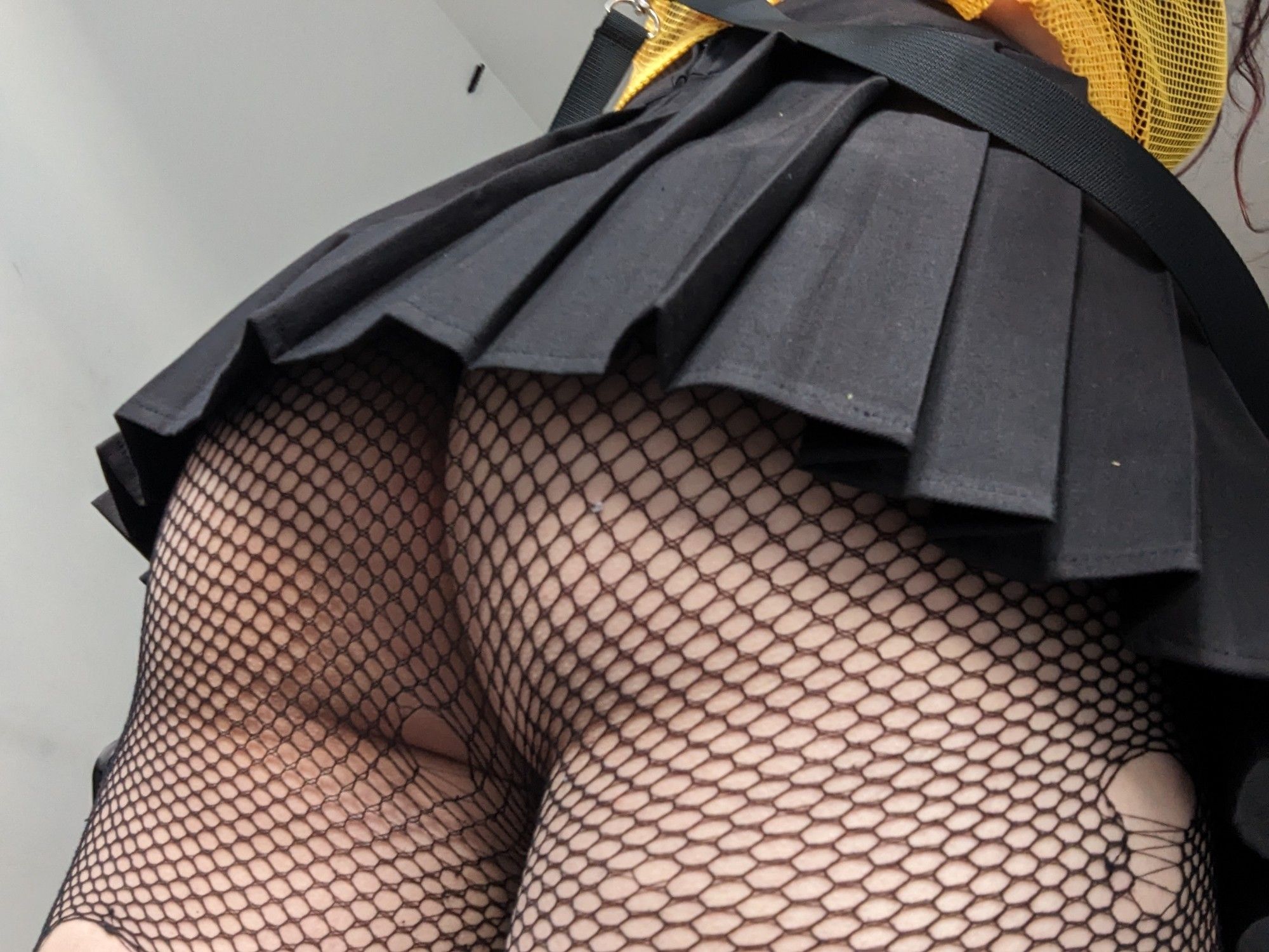 A short black pleated skirt and my butt in slightly ripped fishnet tights