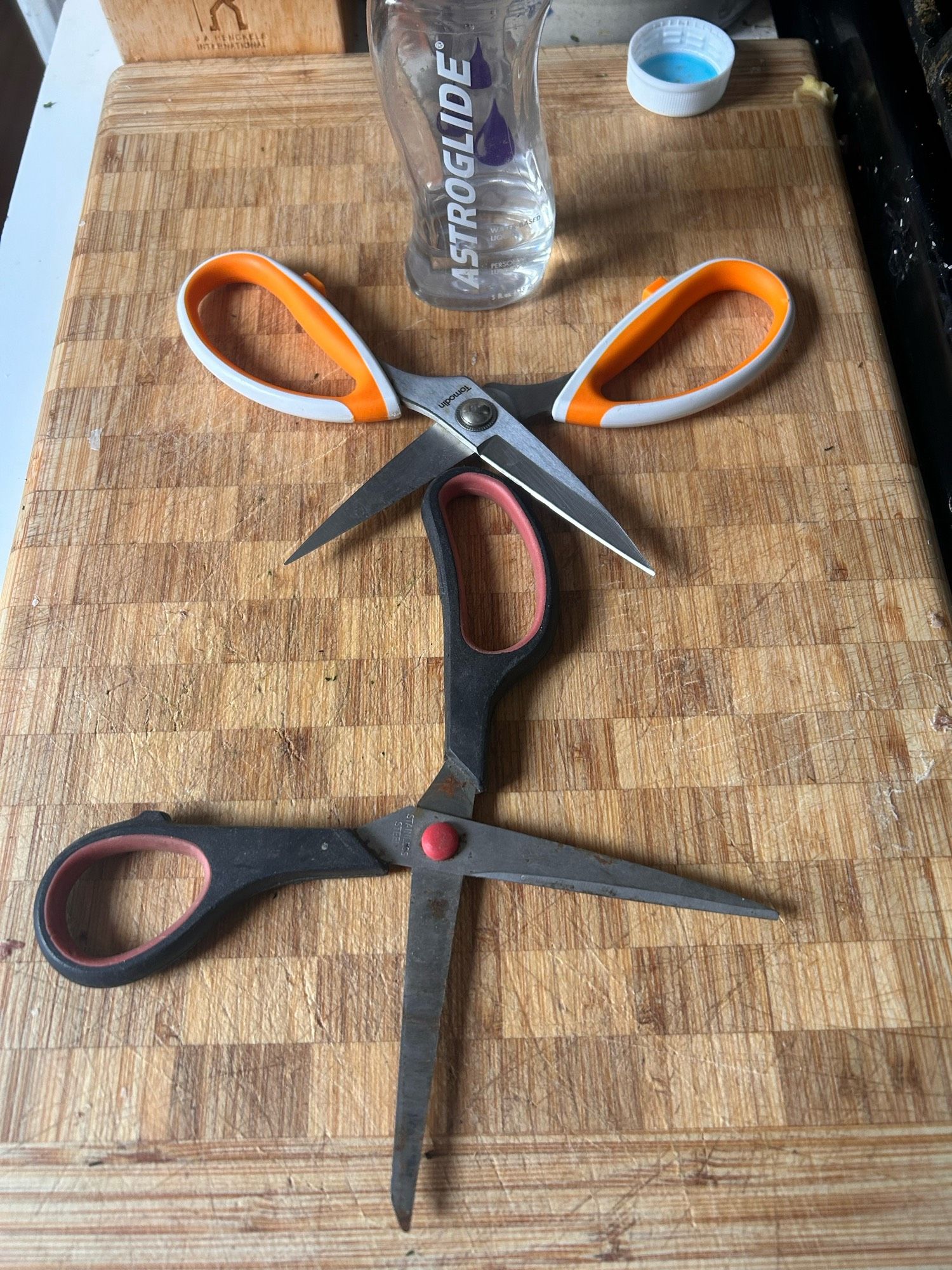 A pair of scissors going down on another pair of scissors on a cutting board, astroglide in the background