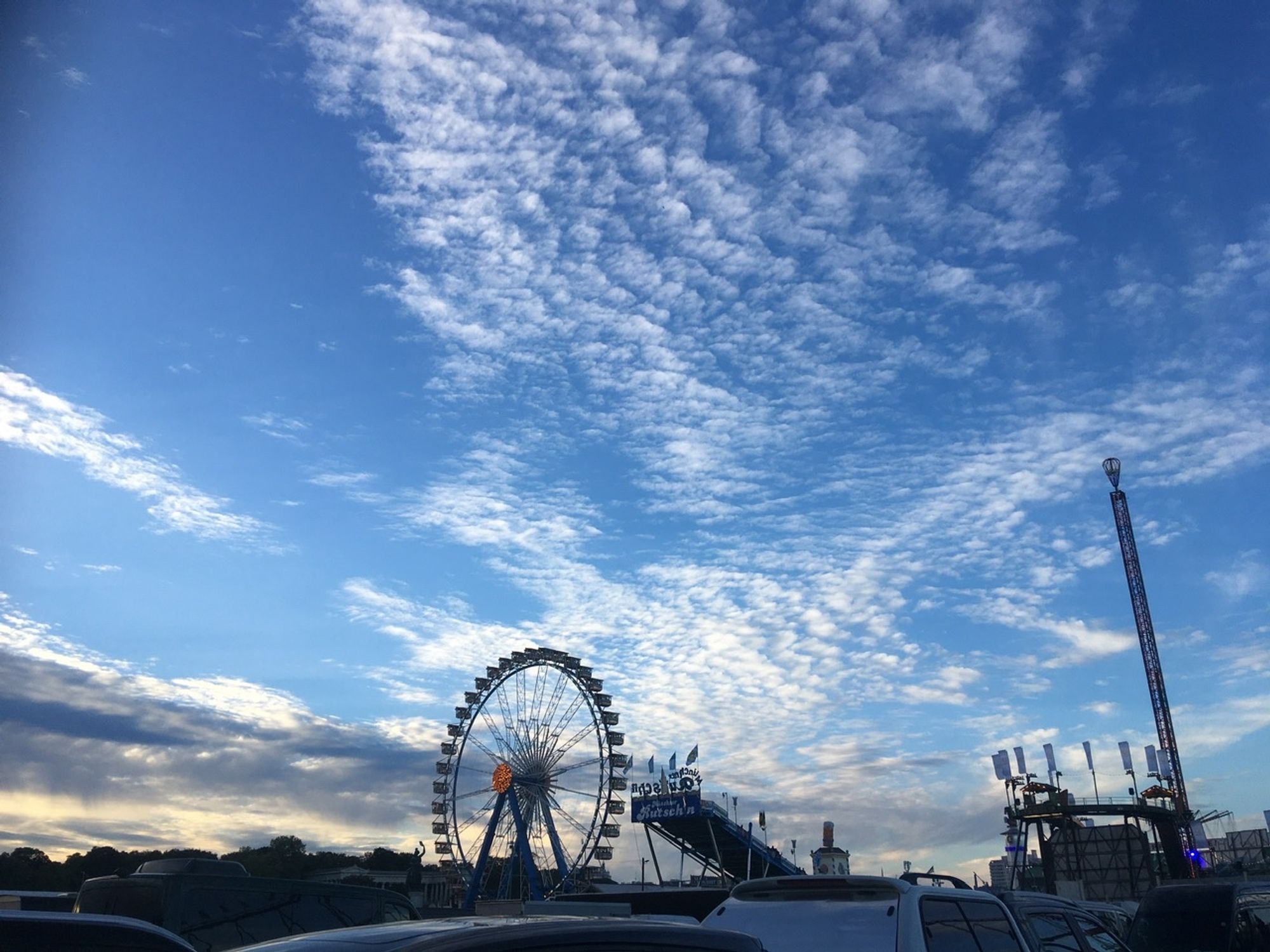 Riesenrad auf dem Oktoberfest unter weißen Wolken am frühabendlichen Münchner Himmel.