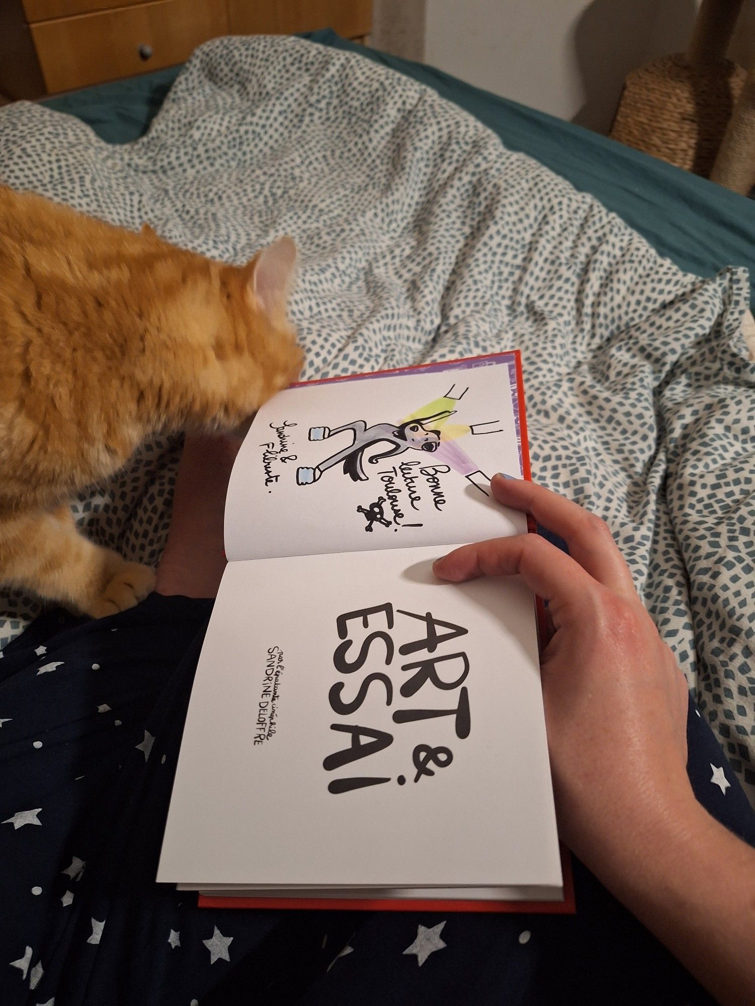 Photo de Toulouse se frottant la tête contre un livre. Il s'agit du Livre Art et Essai de Sandrine Deloffre. On voit sur la page de gauche un chien posant sous les projecteurs comme une rock star. Il souhaite une bonne lecture à Toulouse